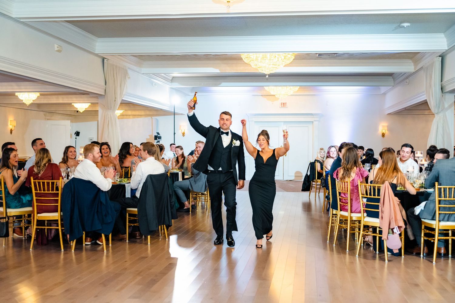 Wide angle shot of an elegant wedding reception showing guests dancing and celebrating in a spacious white ballroom.