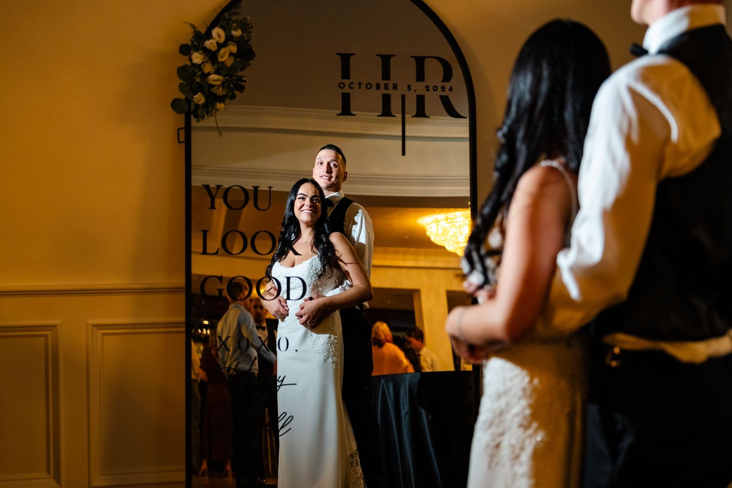 Wedding reception moment captured in warm lighting with decorative text on wall.