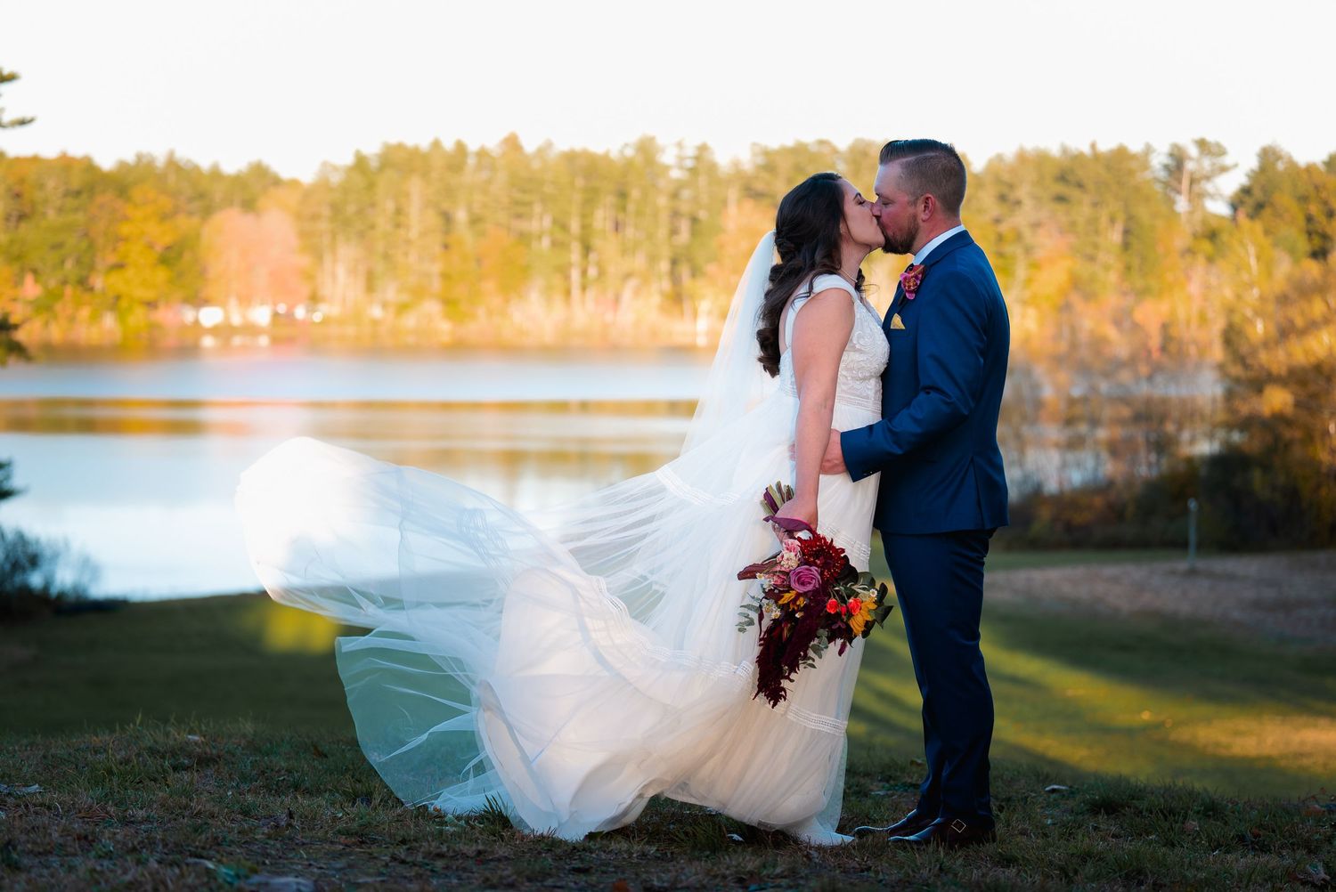 A romantic sunset photoshoot in a golden-lit lakeside setting with flowing white dress and autumn foliage.