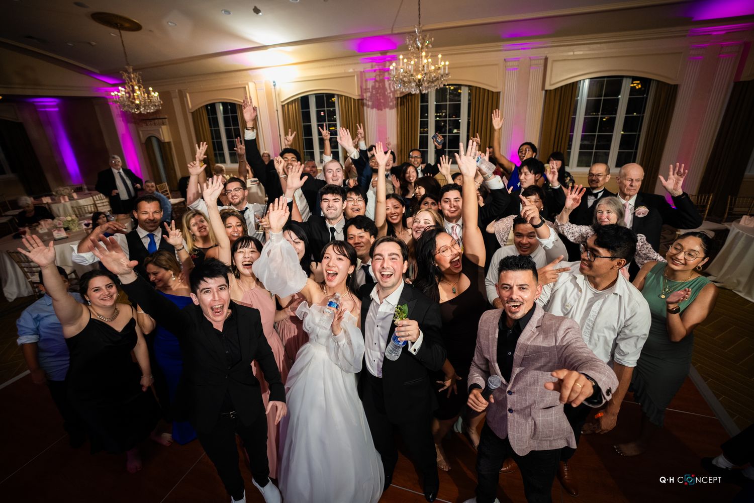 Wedding guests dance and celebrate on a dimly lit dance floor with purple lighting effects.