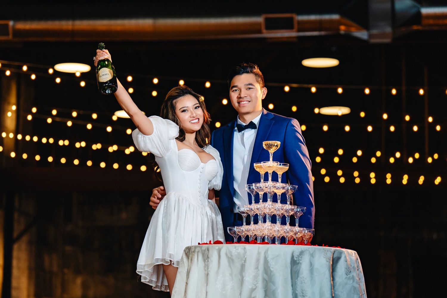 Newlyweds celebrate with multi-tiered wedding cake under string lights.