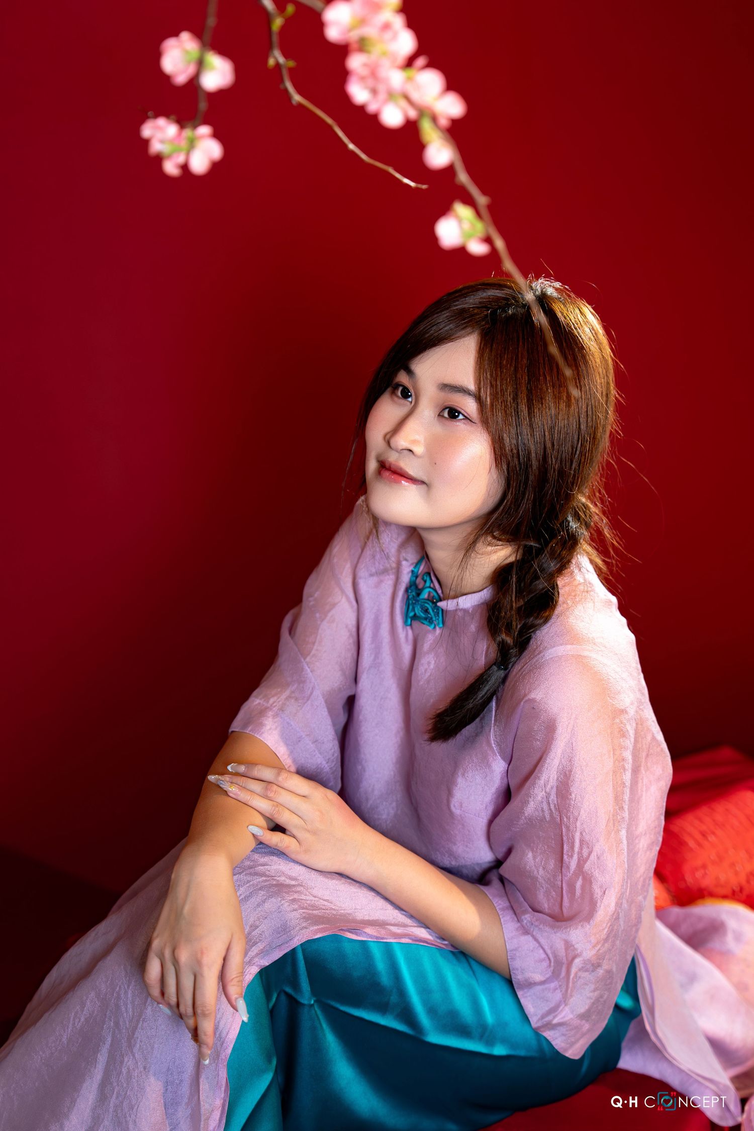 A person in a lavender shirt poses dreamily against a red backdrop with delicate cherry blossom decorations.