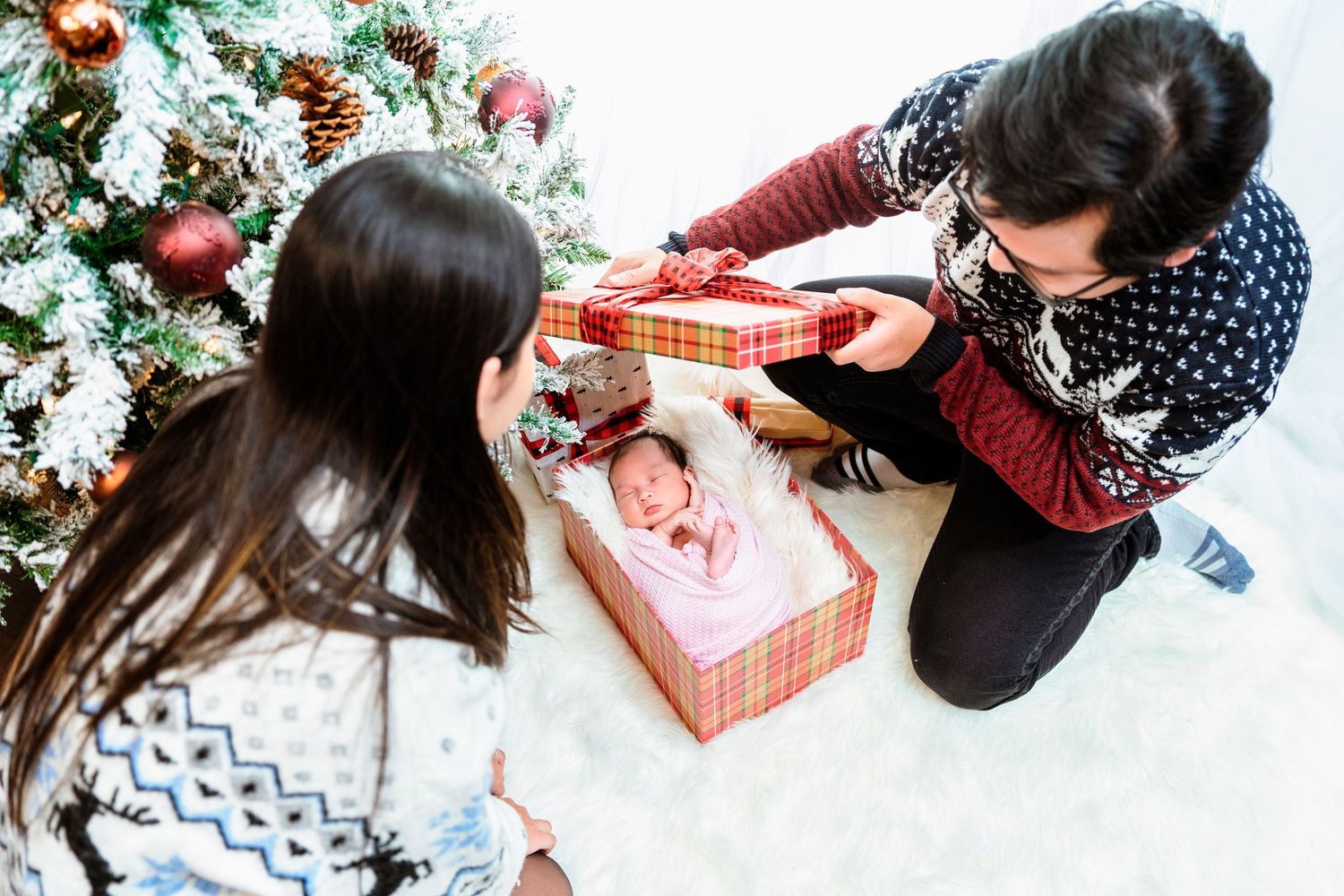Two people opening a Christmas gift box with a newborn baby inside.