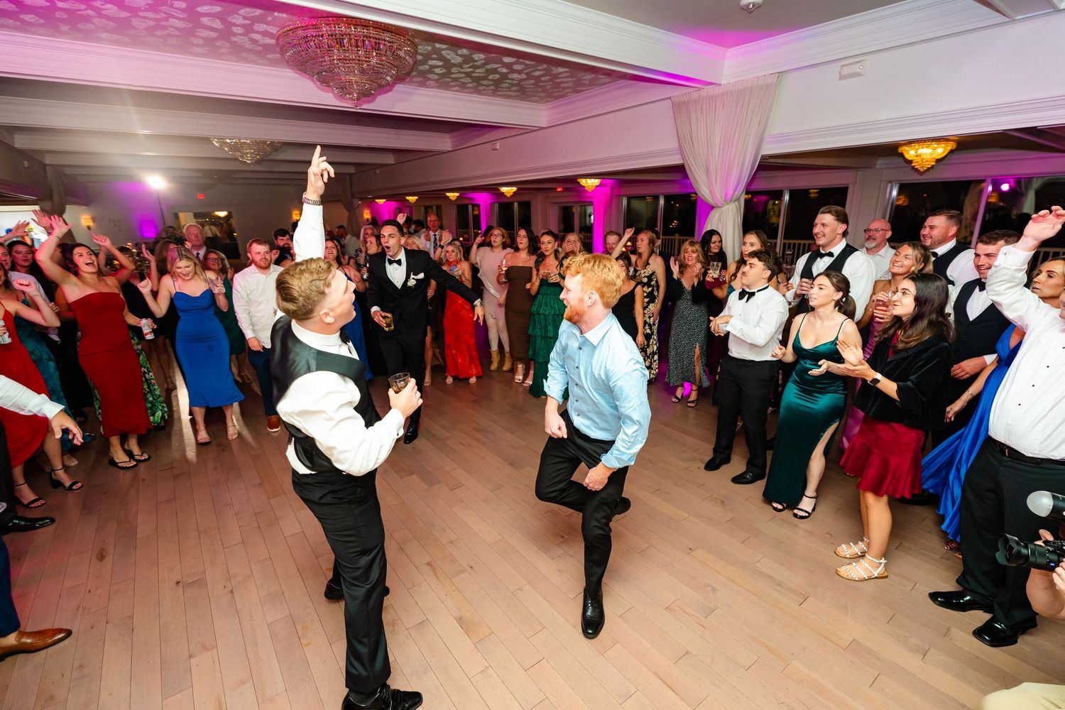 Wedding guests dancing energetically on a pink-lit dance floor during the reception celebration.