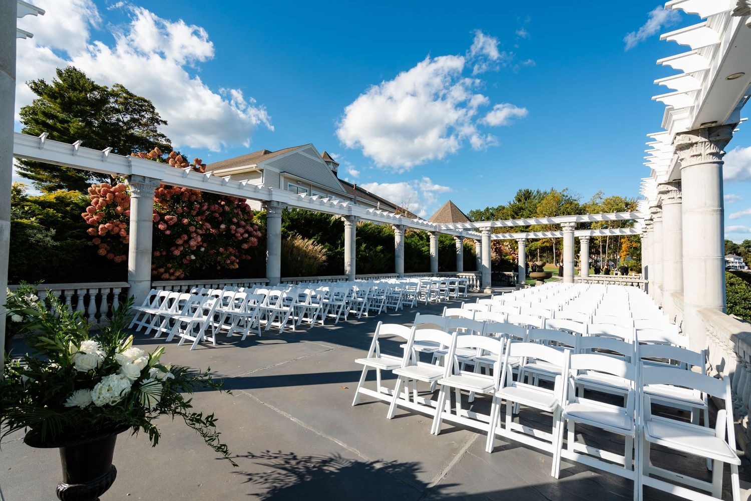 Rows of white wedding chairs set up for an outdoor ceremony under a bright blue sky with fluffy clouds.