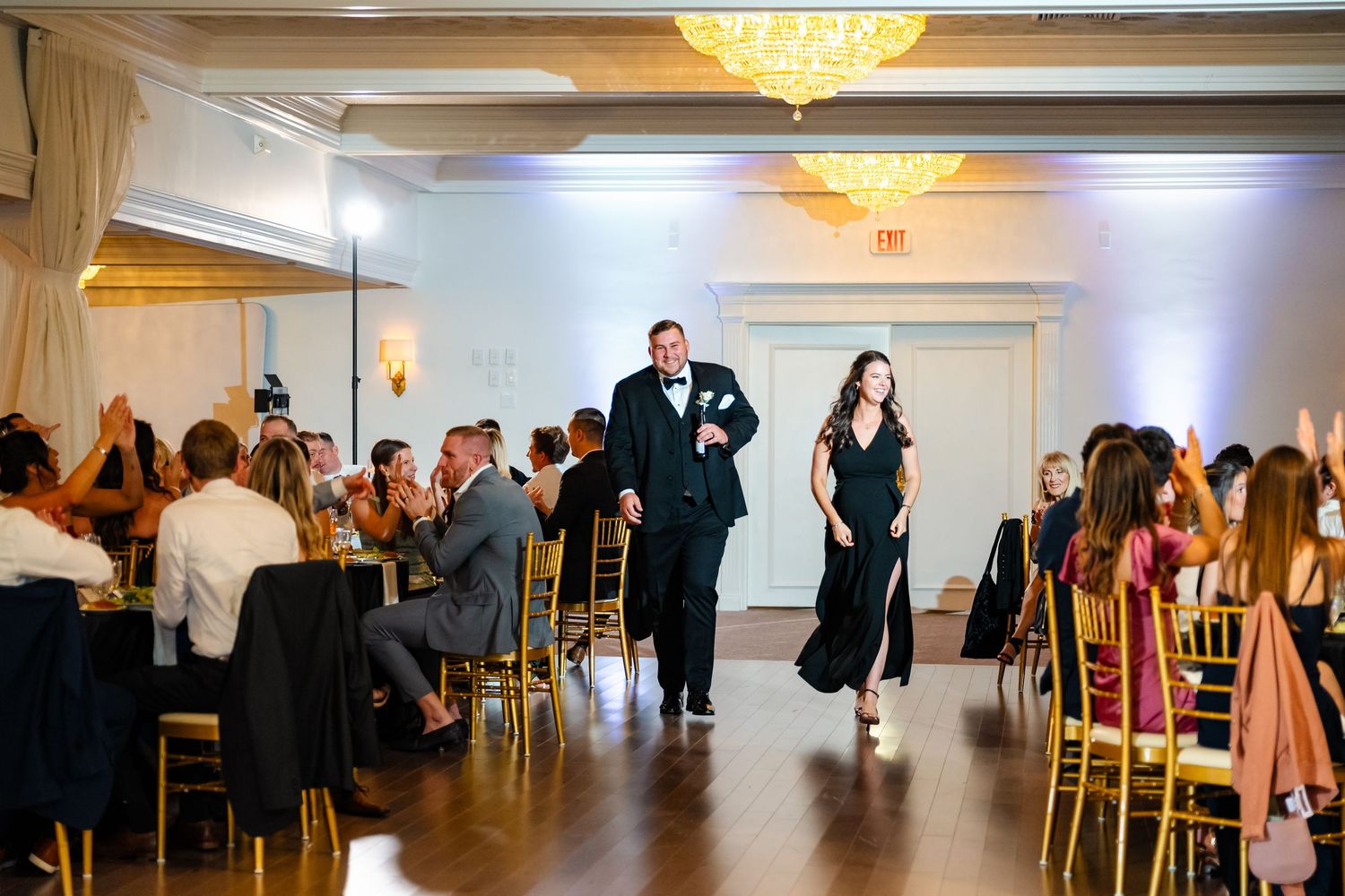 Wedding reception guests dancing and mingling in an elegant ballroom with crystal chandeliers.