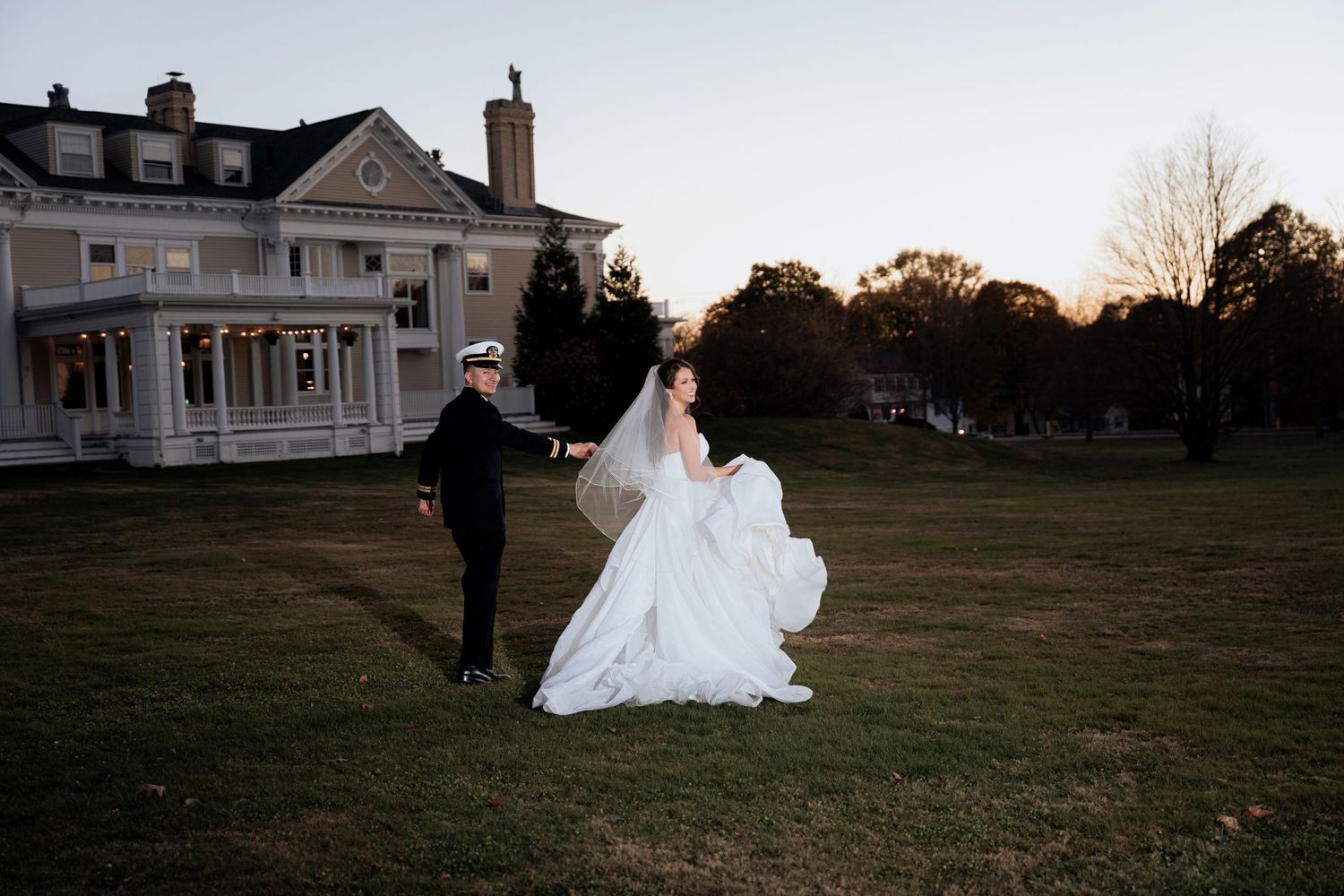Bride in flowing white dress walking across expansive lawn of historic estate.