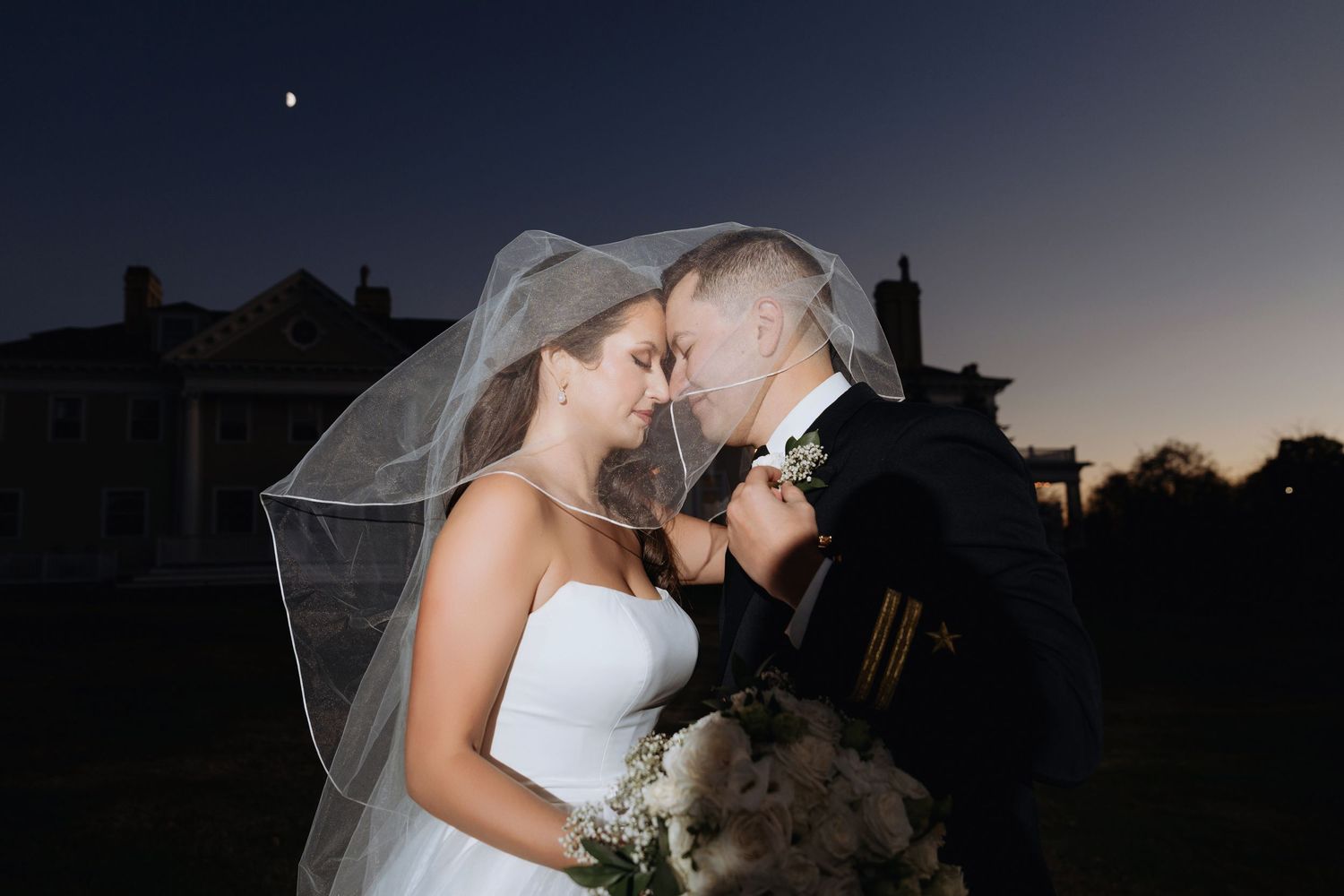 Romantic silhouettes of newlyweds embrace against dusky evening sky.