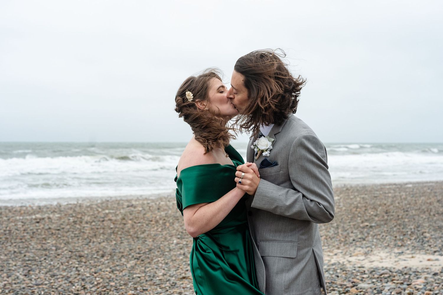 Couple embraces on a stormy beach with dramatic waves crashing in the background.