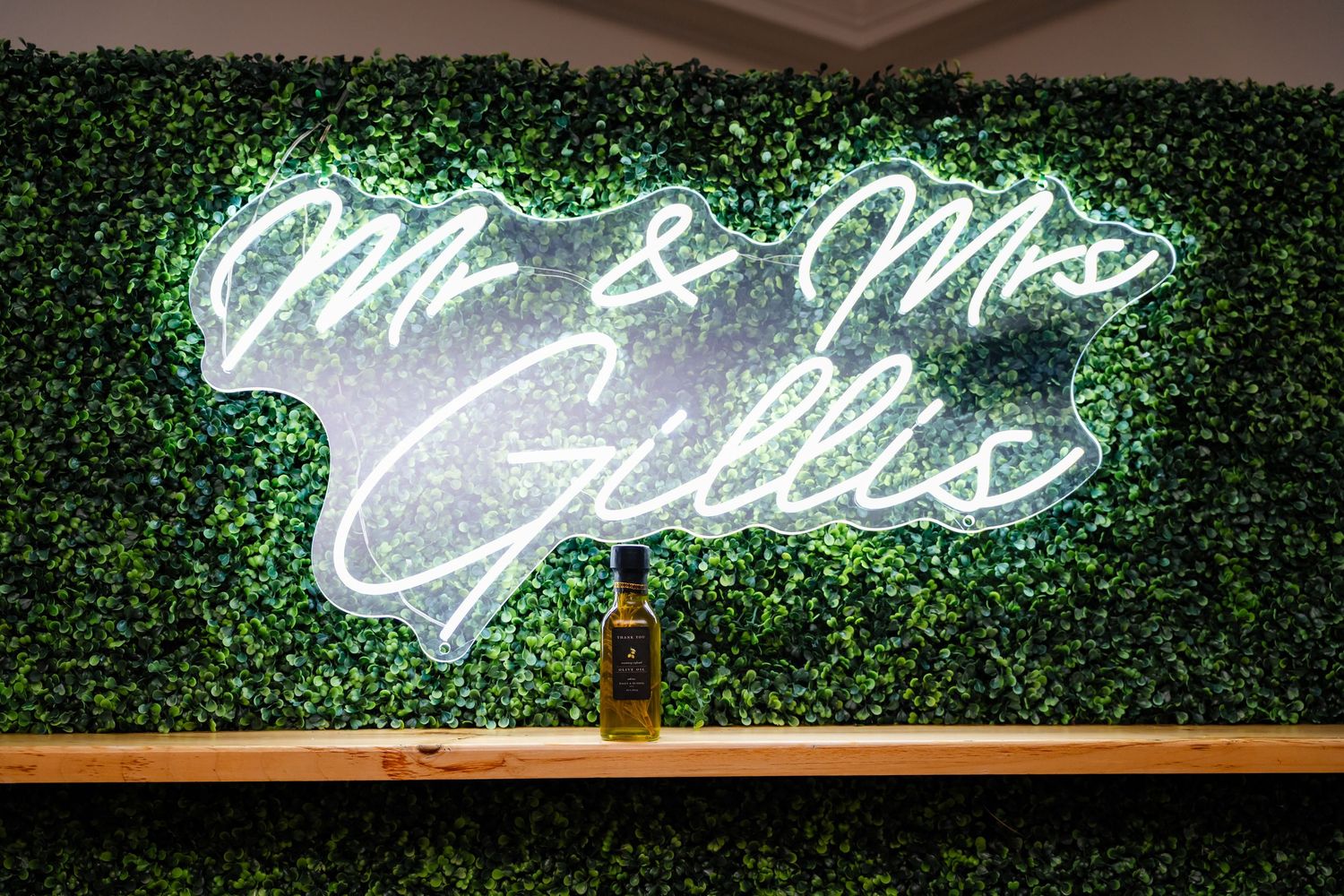 Neon 'Mr & Mrs' sign glowing against a green hedge wall backdrop at a wedding reception.