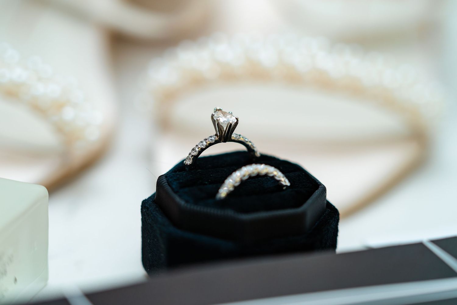 Close-up shots of diamond engagement rings displayed on soft white surfaces.