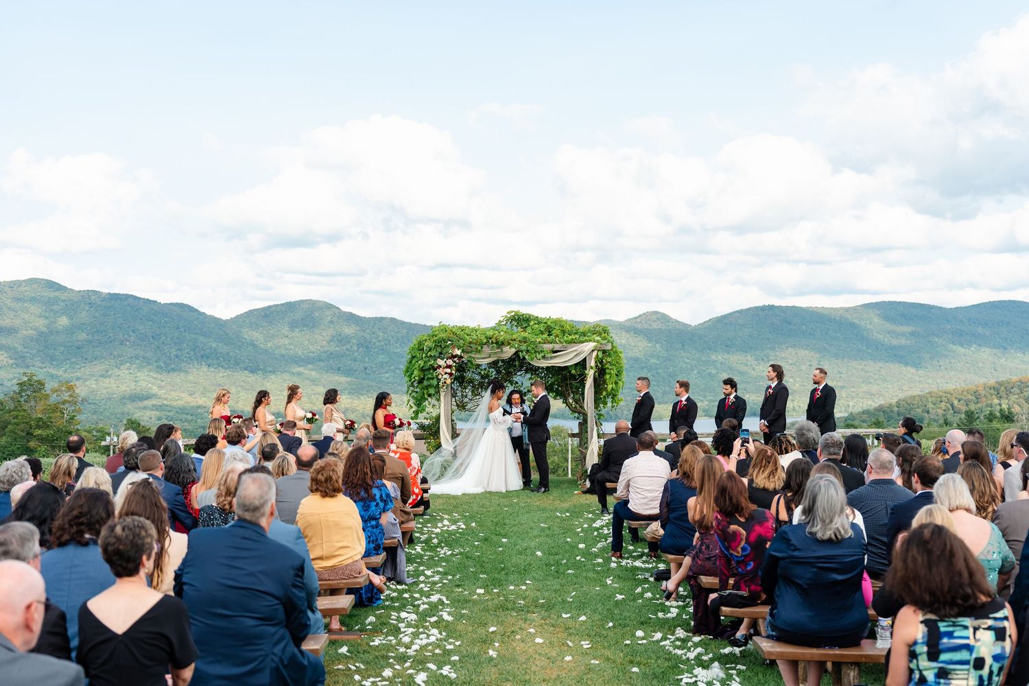 Wedding guests seated outdoors watching ceremony with mountain landscape views.