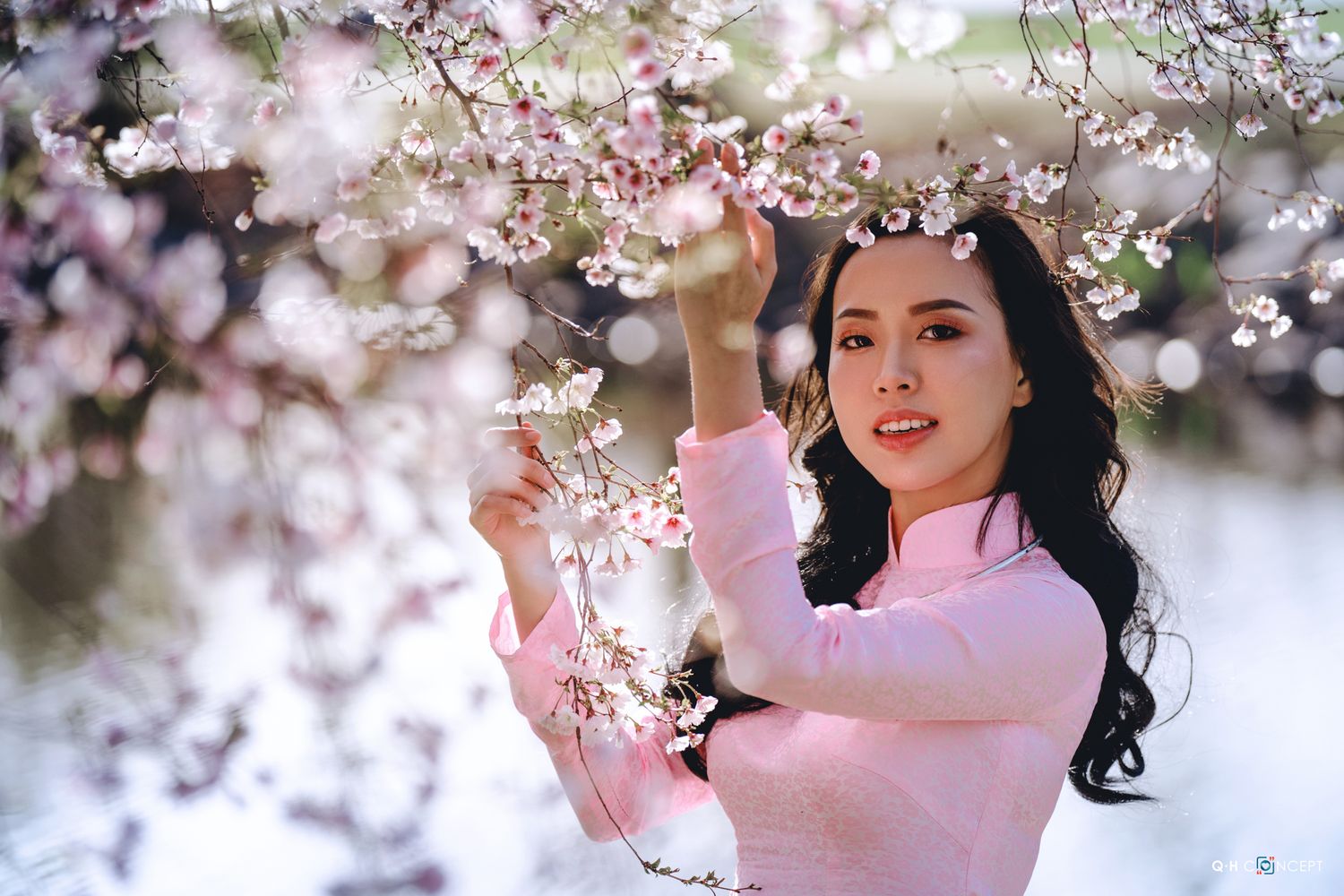A woman in a pink dress poses among blooming cherry blossom trees during spring.
