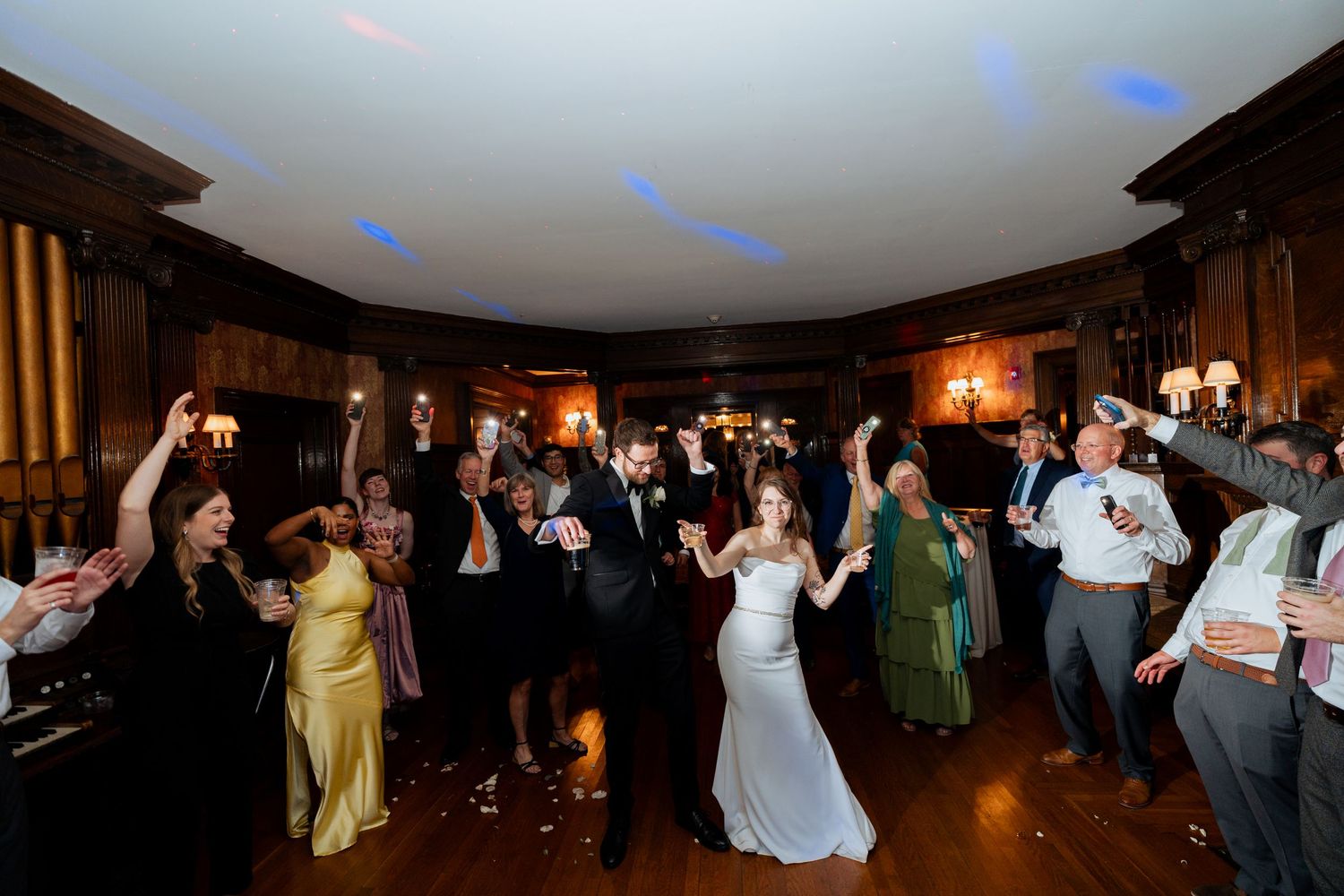Guests dancing and celebrating at a wedding reception with colorful lighting effects.