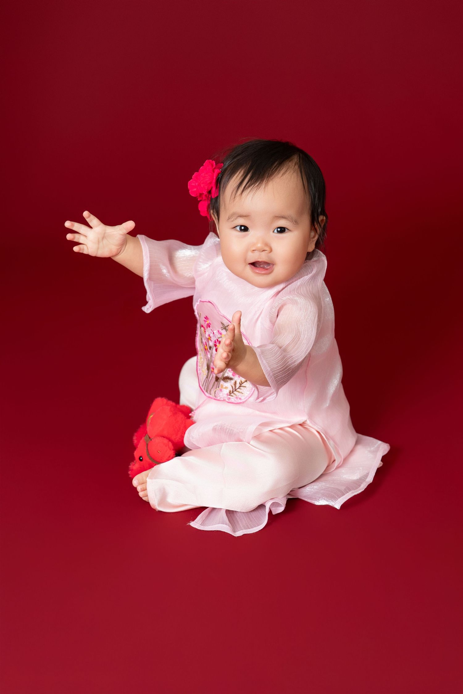 A happy baby in a pink dress poses against a deep red background in a series of playful studio portraits.