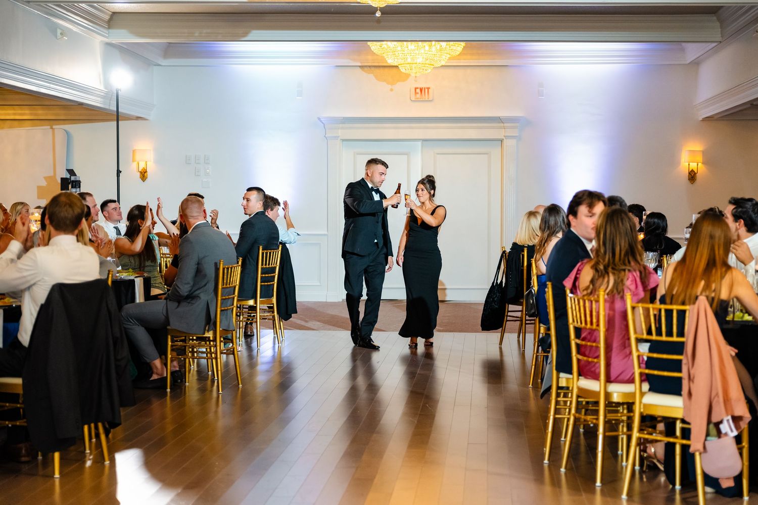 Wedding reception venue with gold chiavari chairs and elegant lighting.