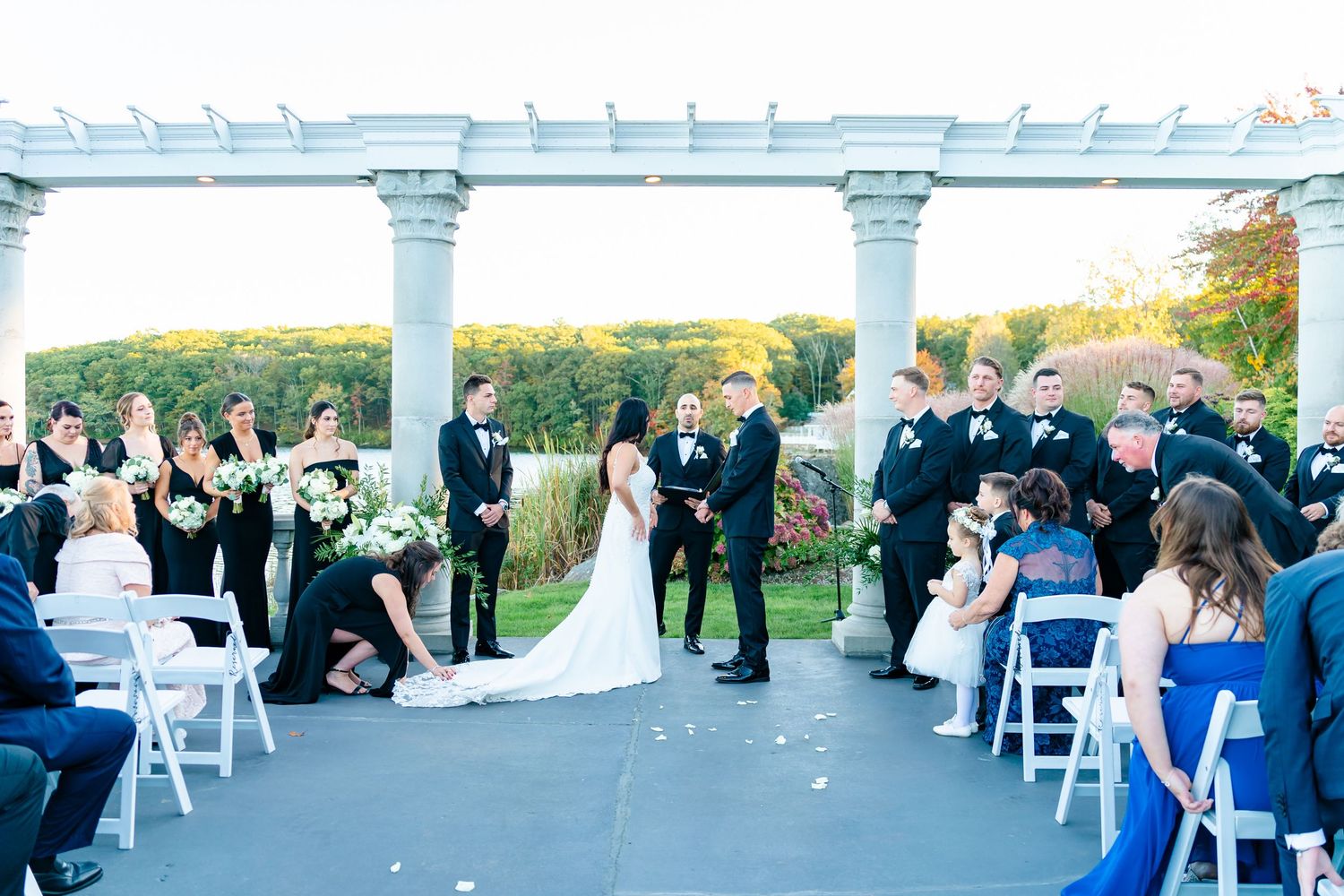 Wide view of outdoor wedding ceremony space with white pergola and chairs set up on a lawn.