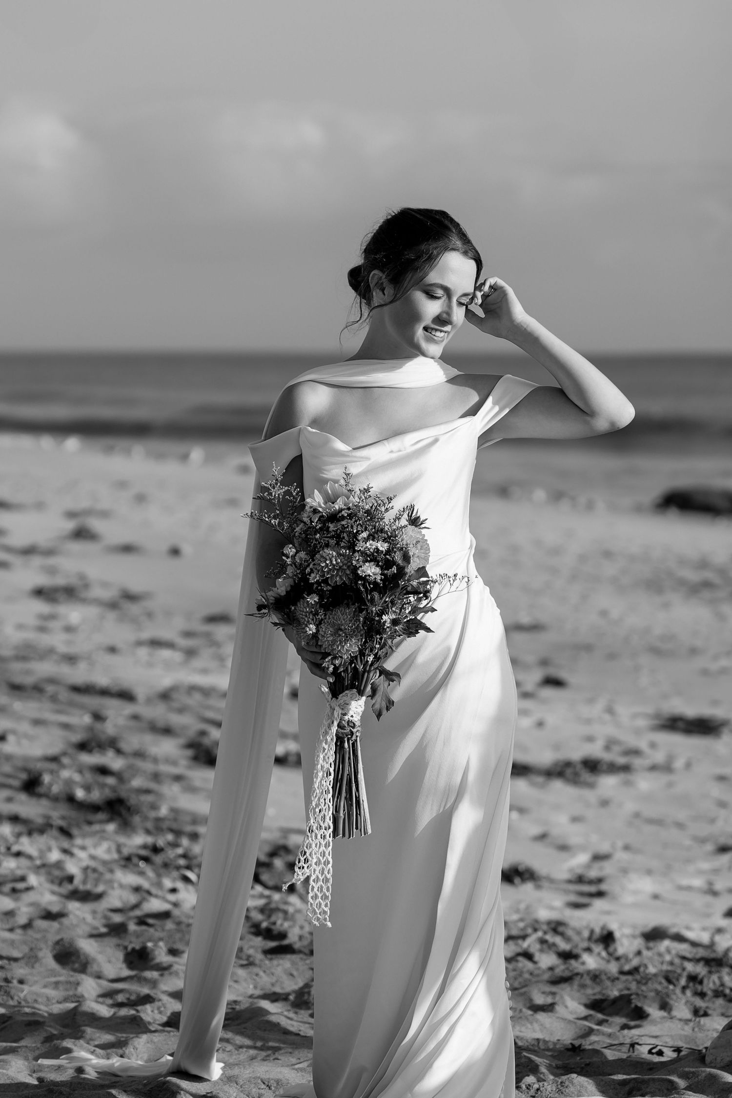 Black and white photos of bride holding bouquet on windswept beach.