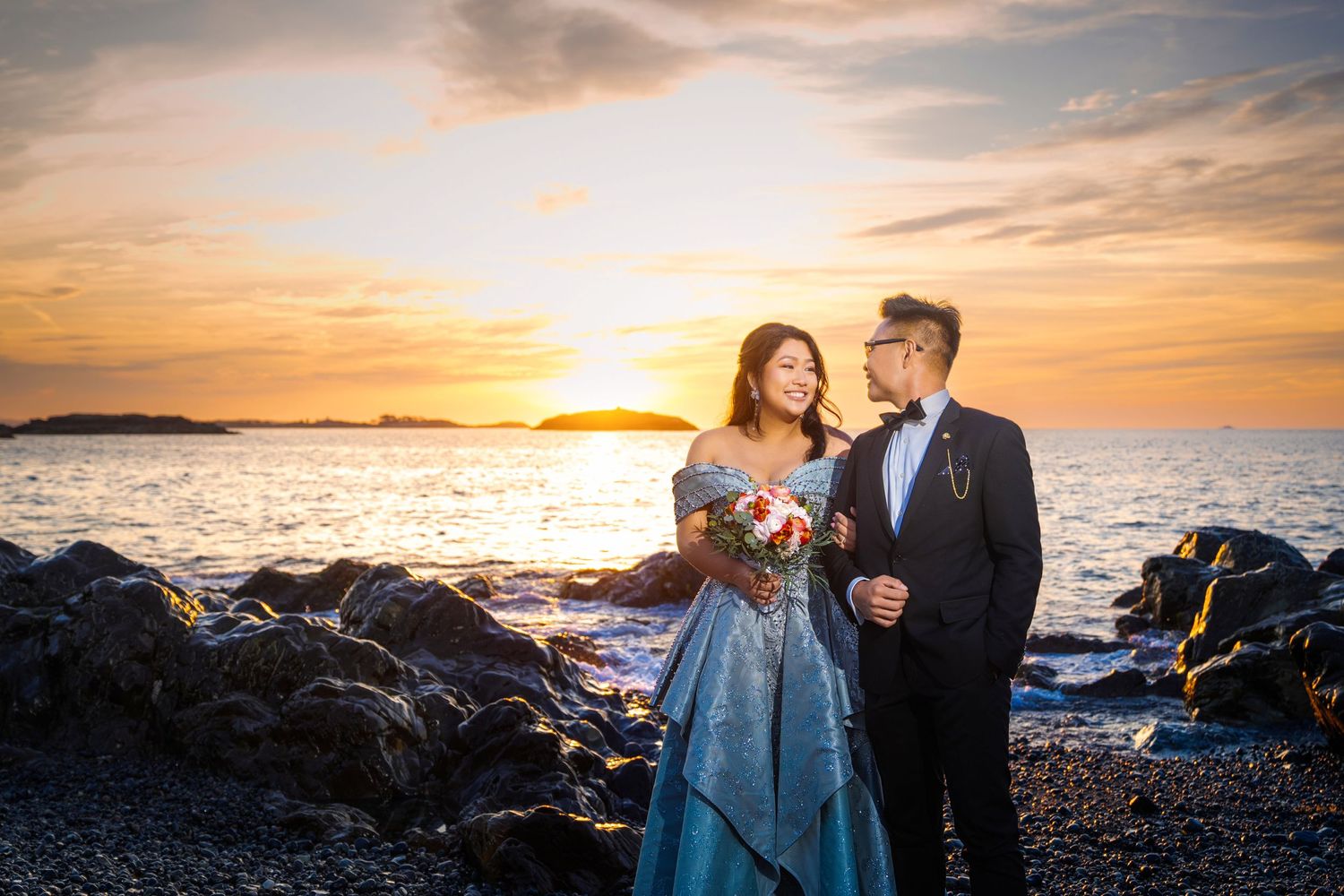 Couple shares intimate moment during golden hour by rocky coastline.