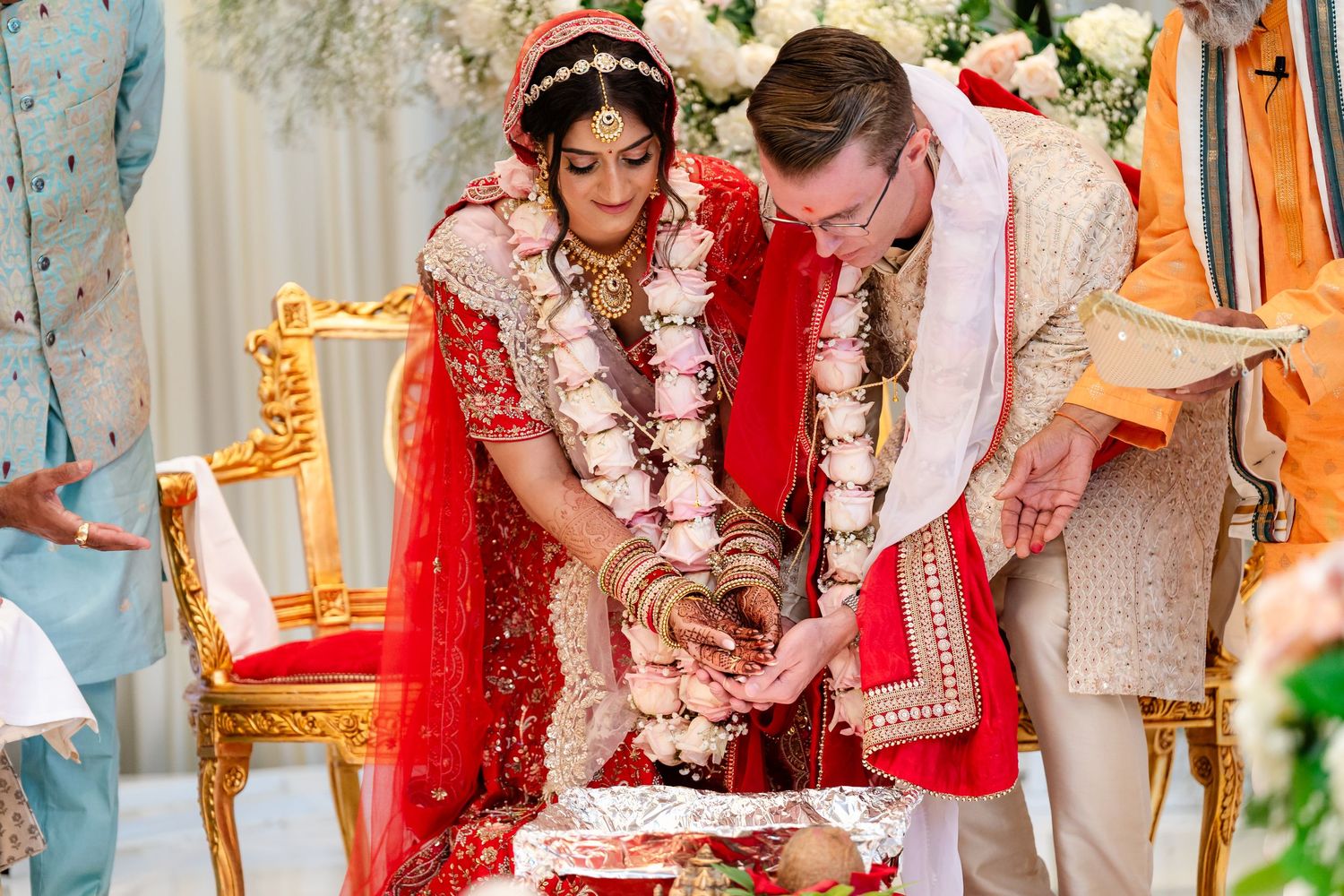 A couple in traditional Indian wedding attire performs ceremonial rituals during their marriage celebration.