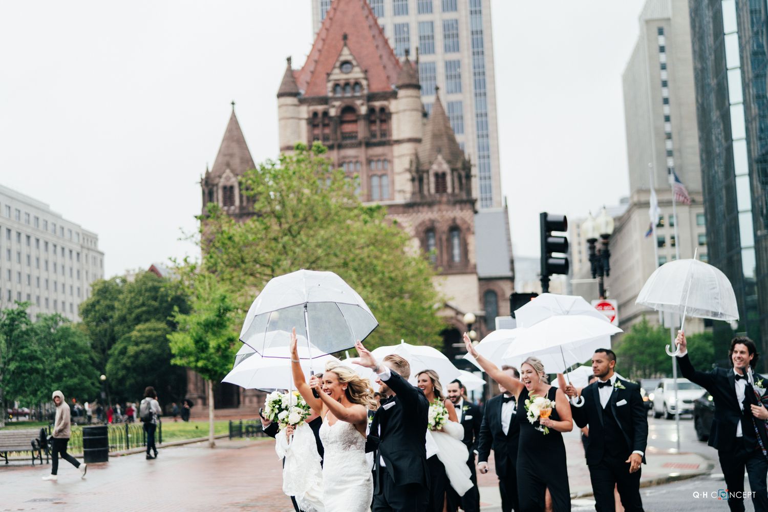 Wedding party poses with white umbrellas in front of Trinity Church in Boston's Copley Square on a cloudy day.