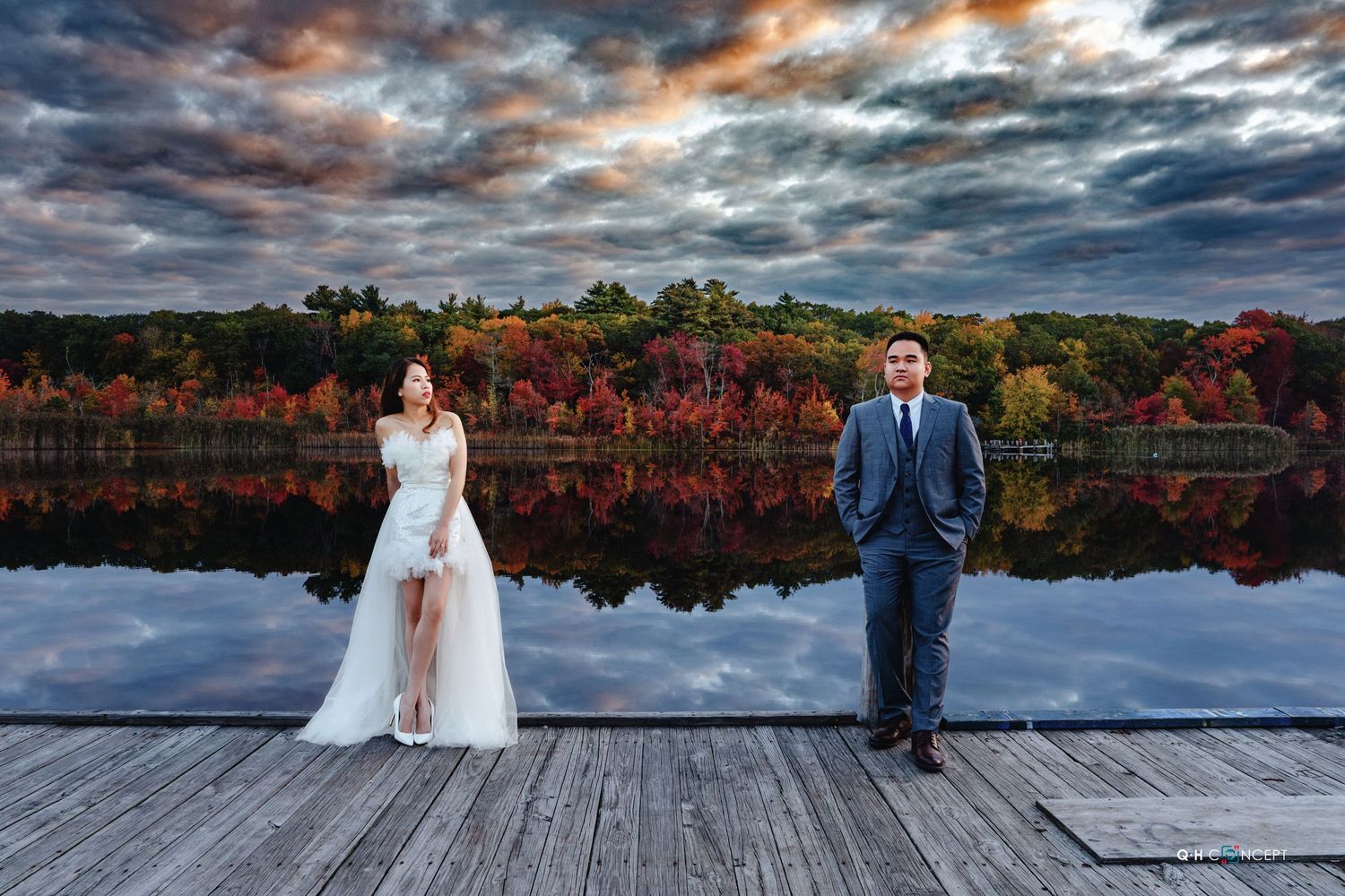 Dramatic sky over lake with wooden dock during autumn wedding photoshoot.