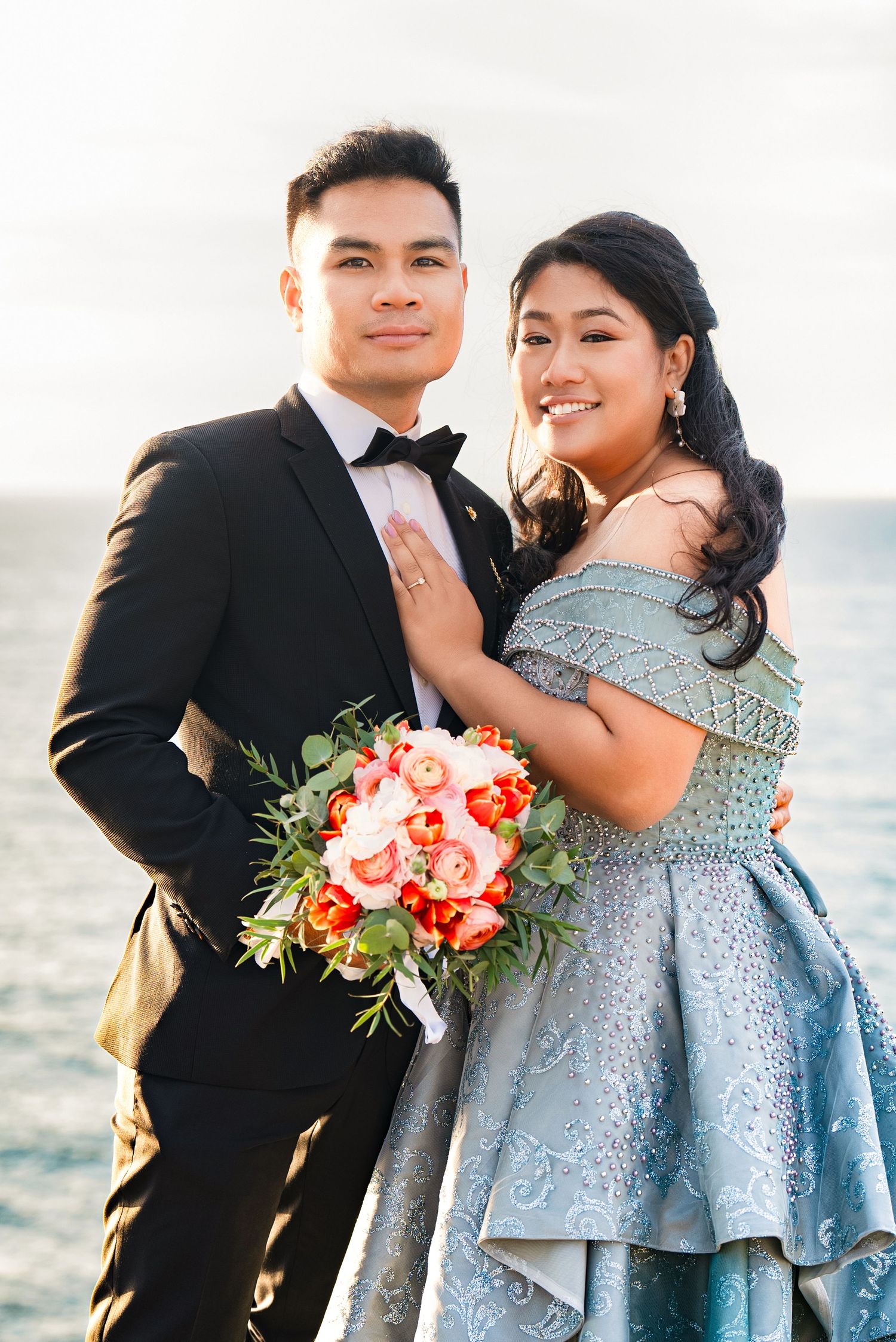 Intimate wedding portraits featuring a blue dress and coral bouquet by the seaside.
