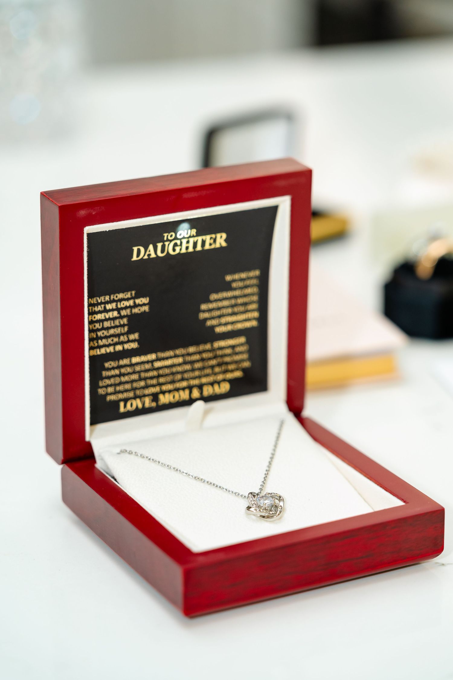 Red jewelry box displaying a delicate necklace with sentimental message to daughter.