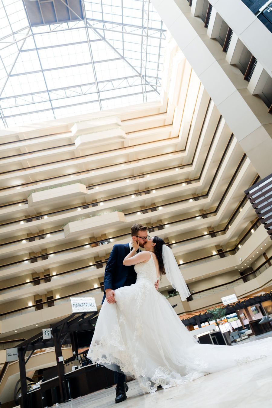 Dramatic wedding photo in modern atrium with angular white architecture and romantic dip pose.