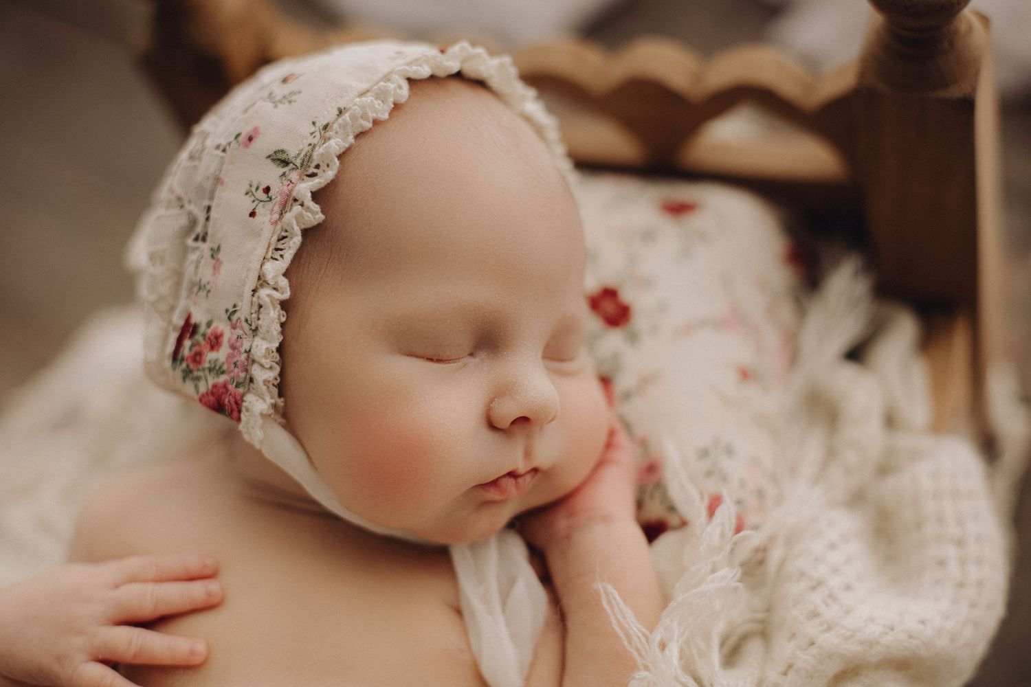 Sleeping baby in lace bonnet resting on floral textured fabric.