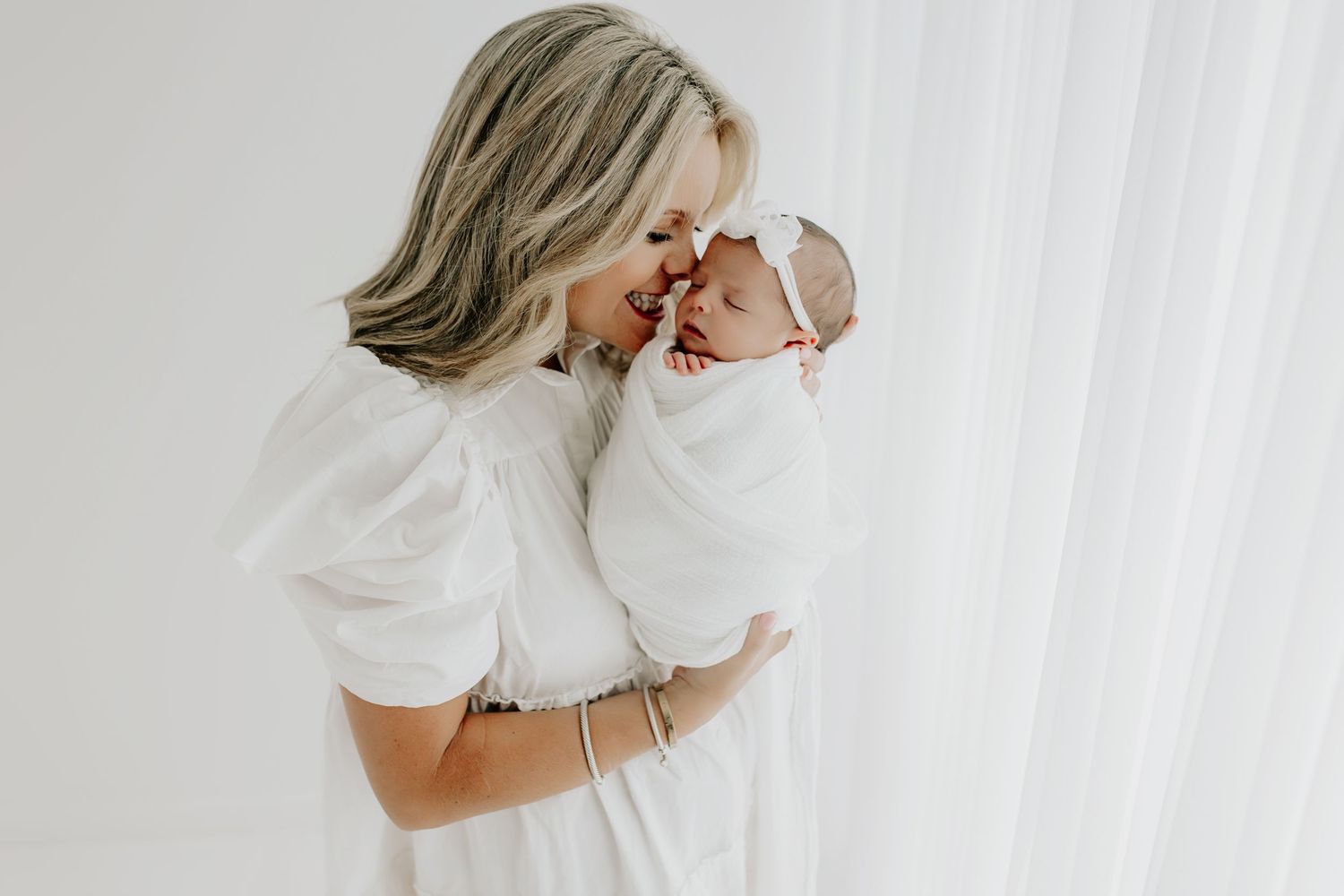 Parent in white holds newborn close in tender moment by window.