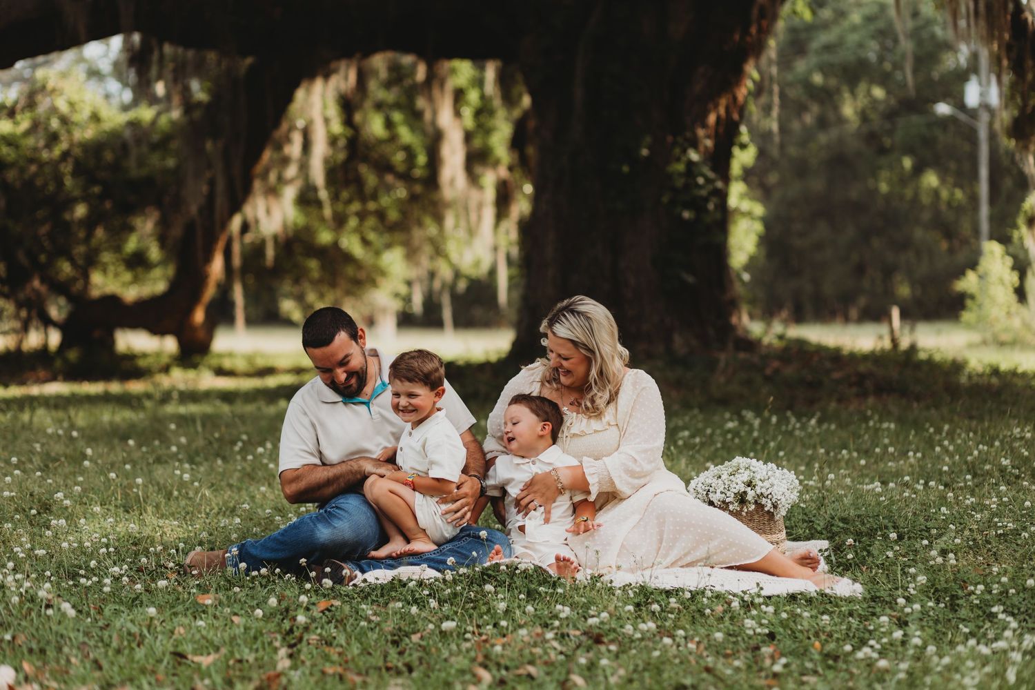 Family relaxes together on white blanket during outdoor photo session with wildflowers.