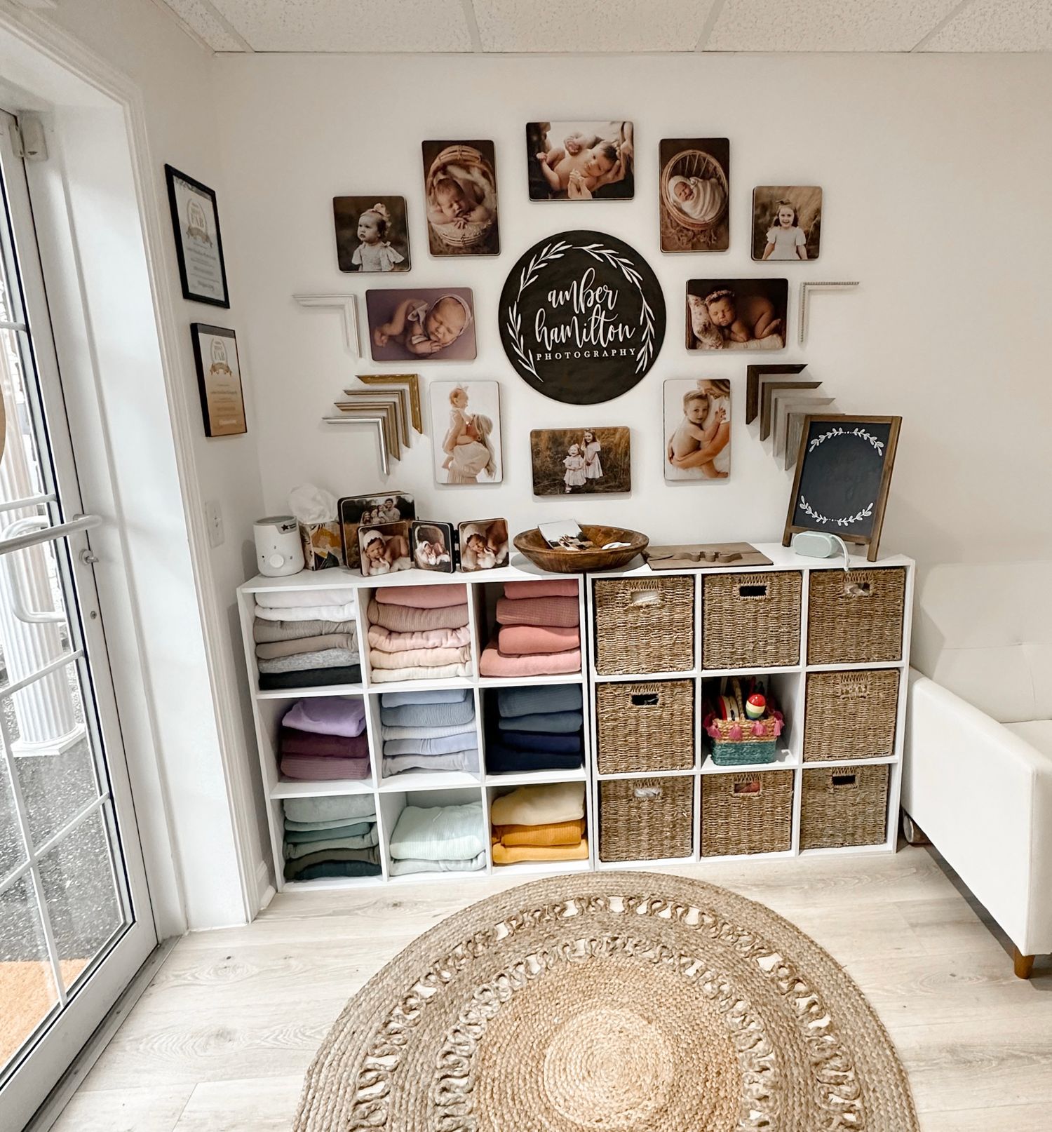 Organized photography studio storage with cubby shelves, textiles, and a gallery wall of portrait prints.