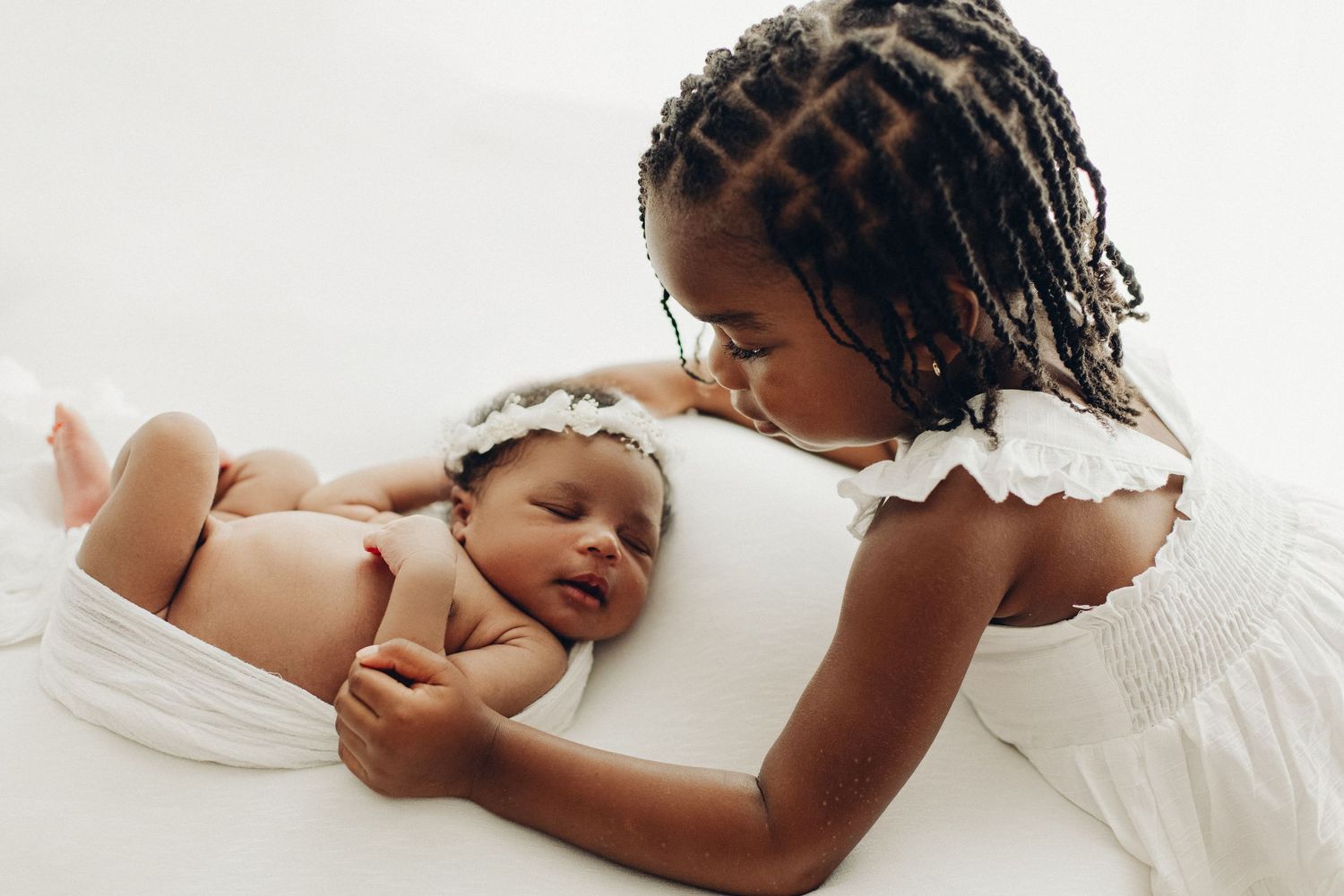 Sweet moment between person in white dress and newborn baby on white background.