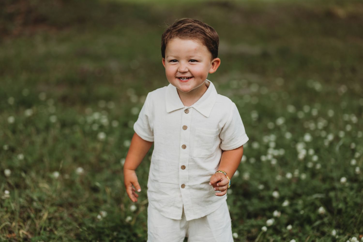 Child laughs joyfully while wearing all white clothing in a flower-filled meadow.
