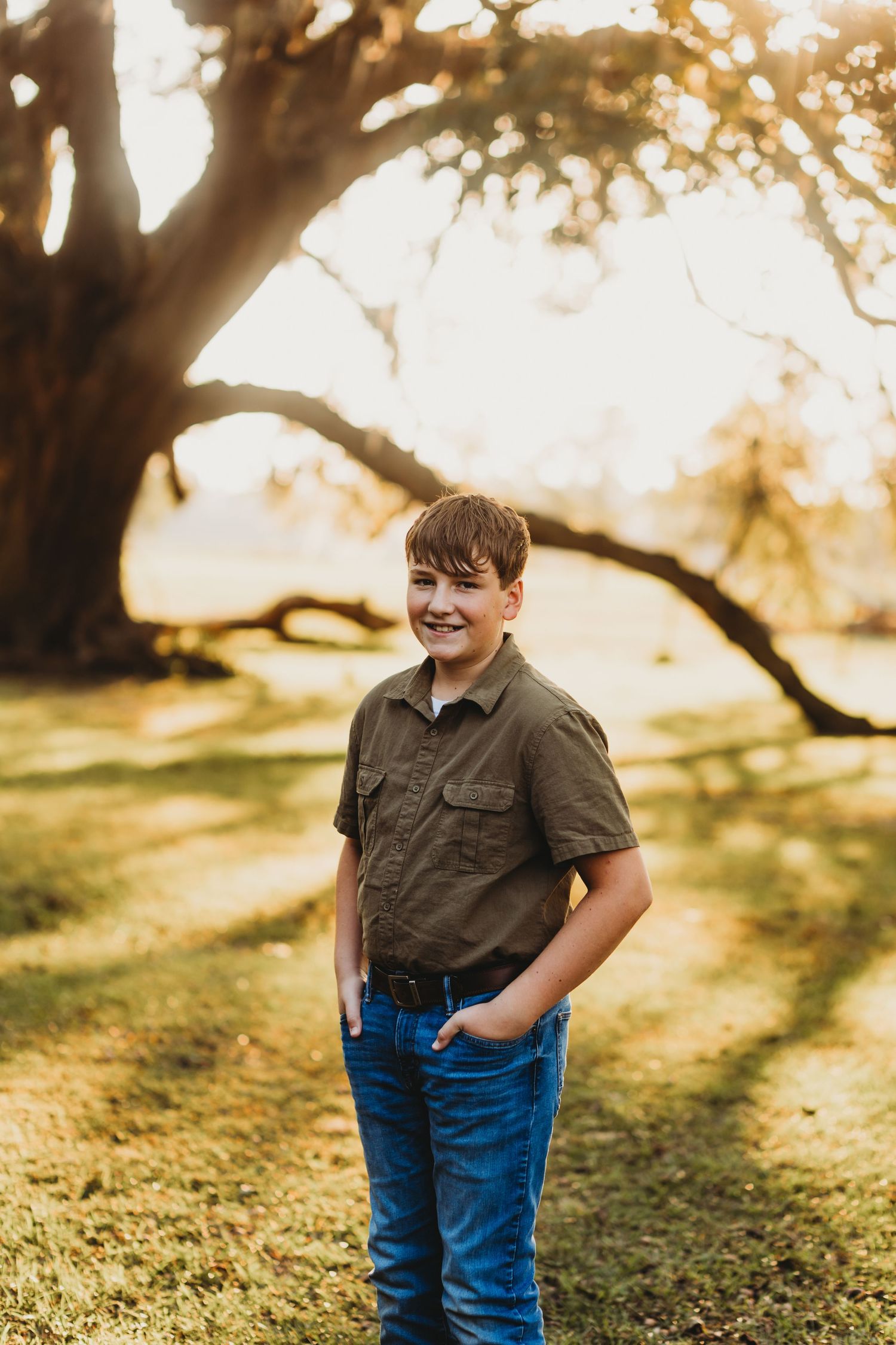 Portrait of young person in olive shirt and jeans standing in golden sunlit setting.
