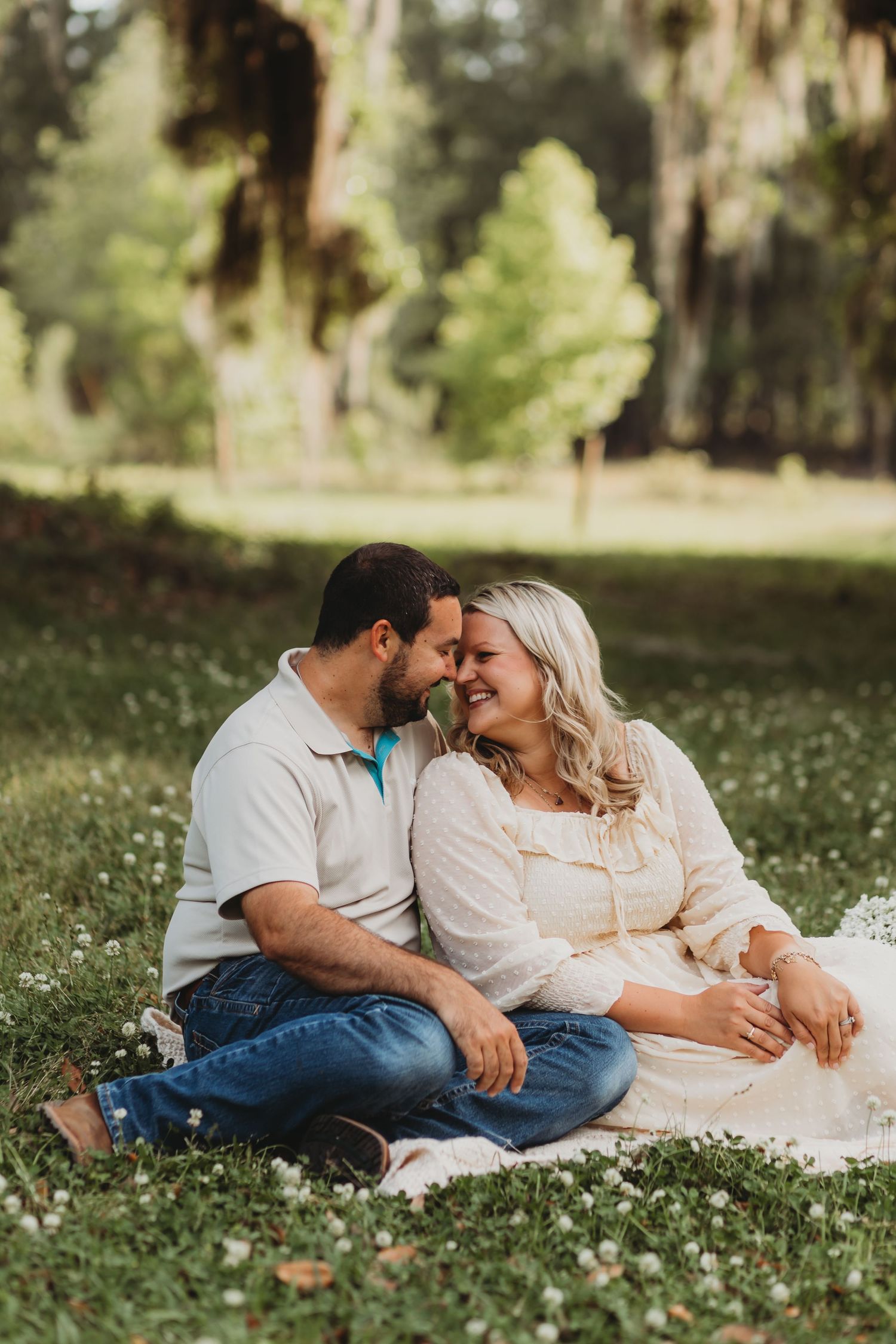 Couple shares intimate moment while lying on blanket in field of white flowers.