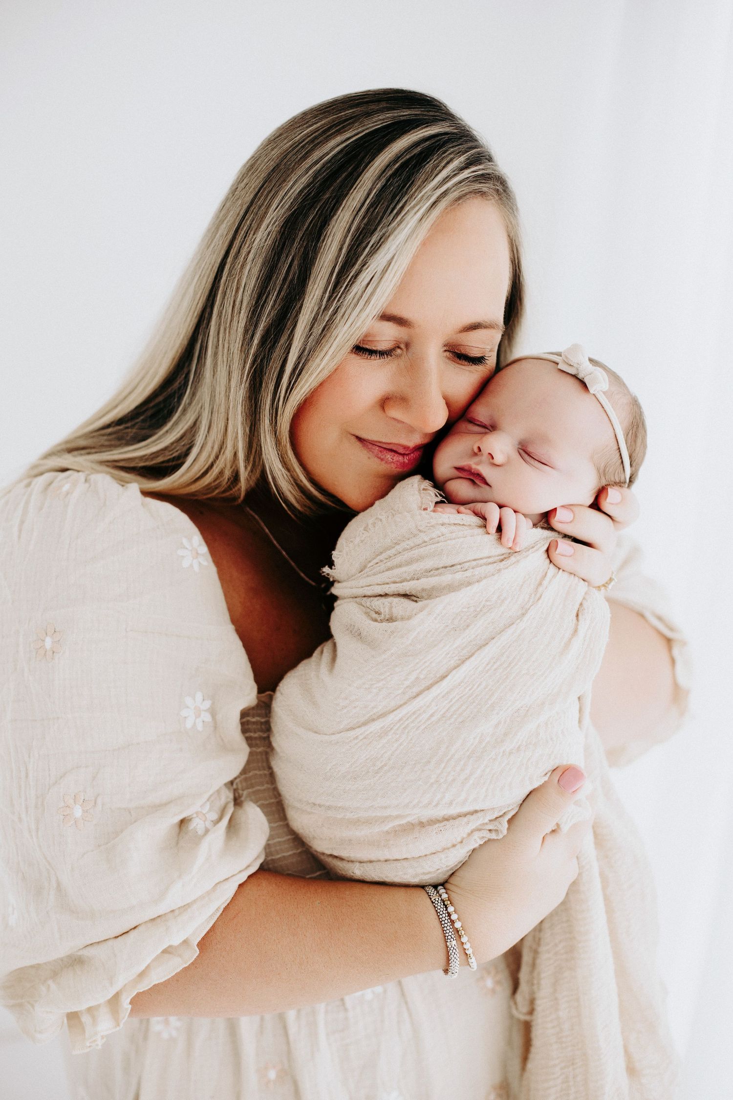 Intimate family moment captured in neutral tones as mother cuddles sleeping newborn.