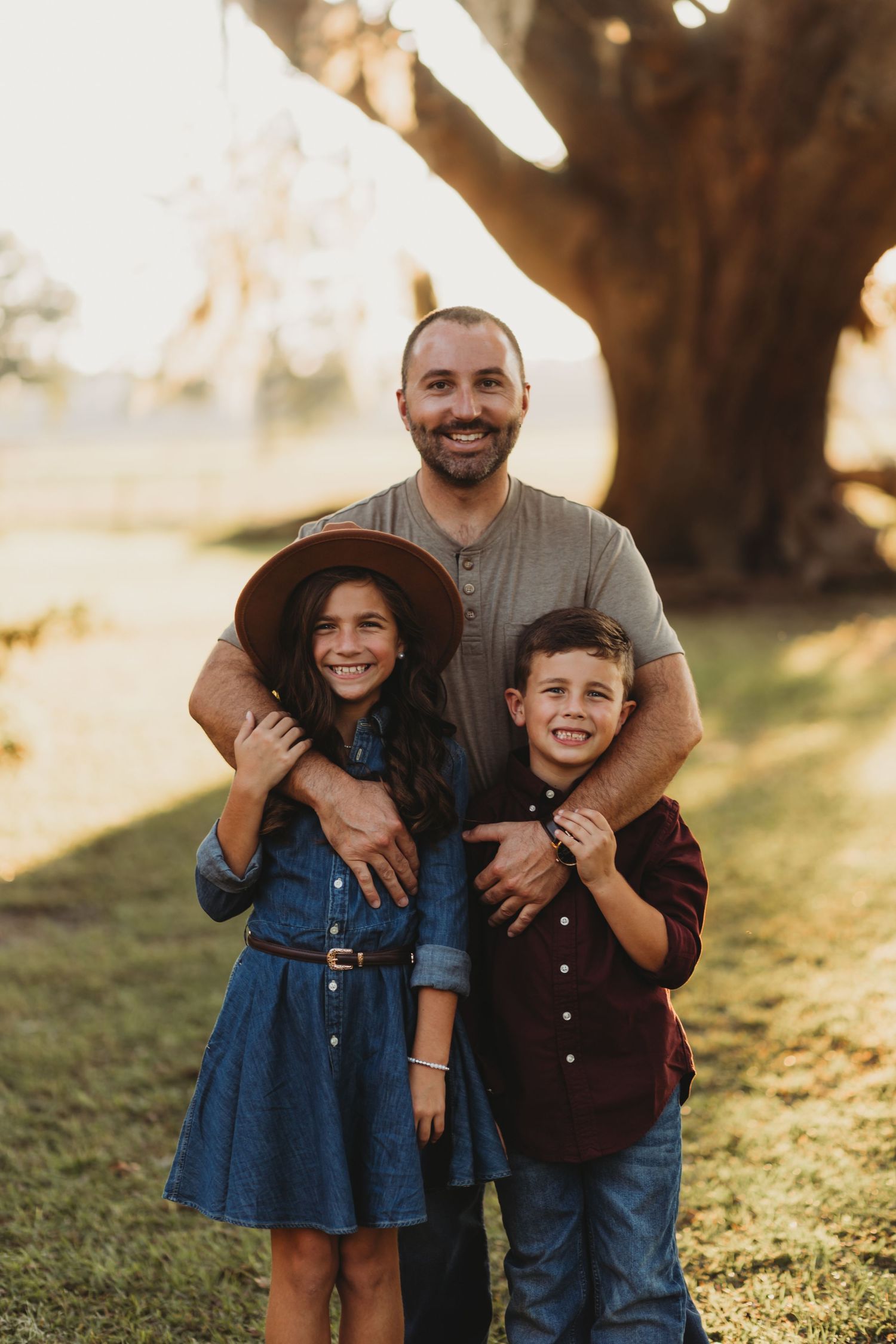 Family of four posing together under large trees during sunset photo session.