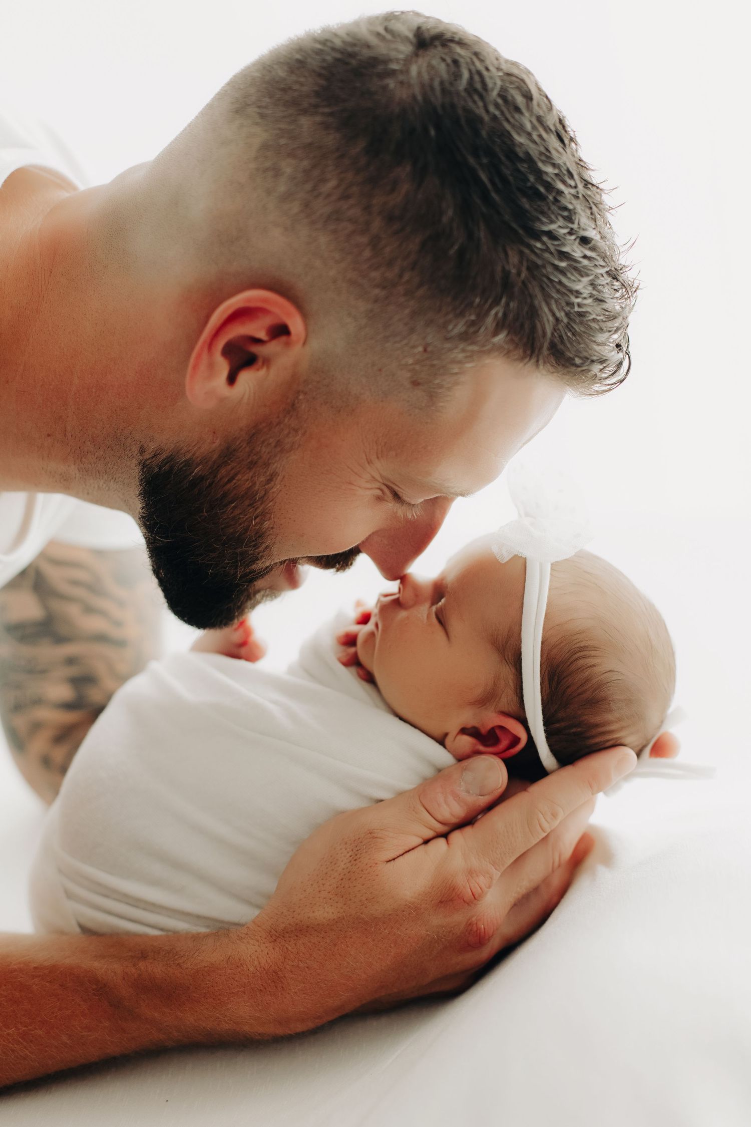 Tender moment between parent and swaddled newborn in white.