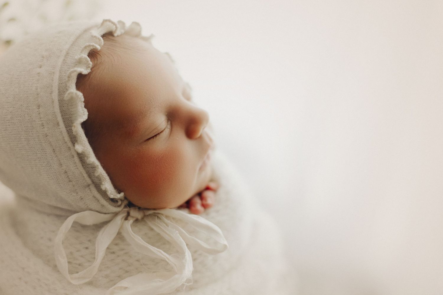 Close-up of sleeping baby in white vintage-style bonnet.