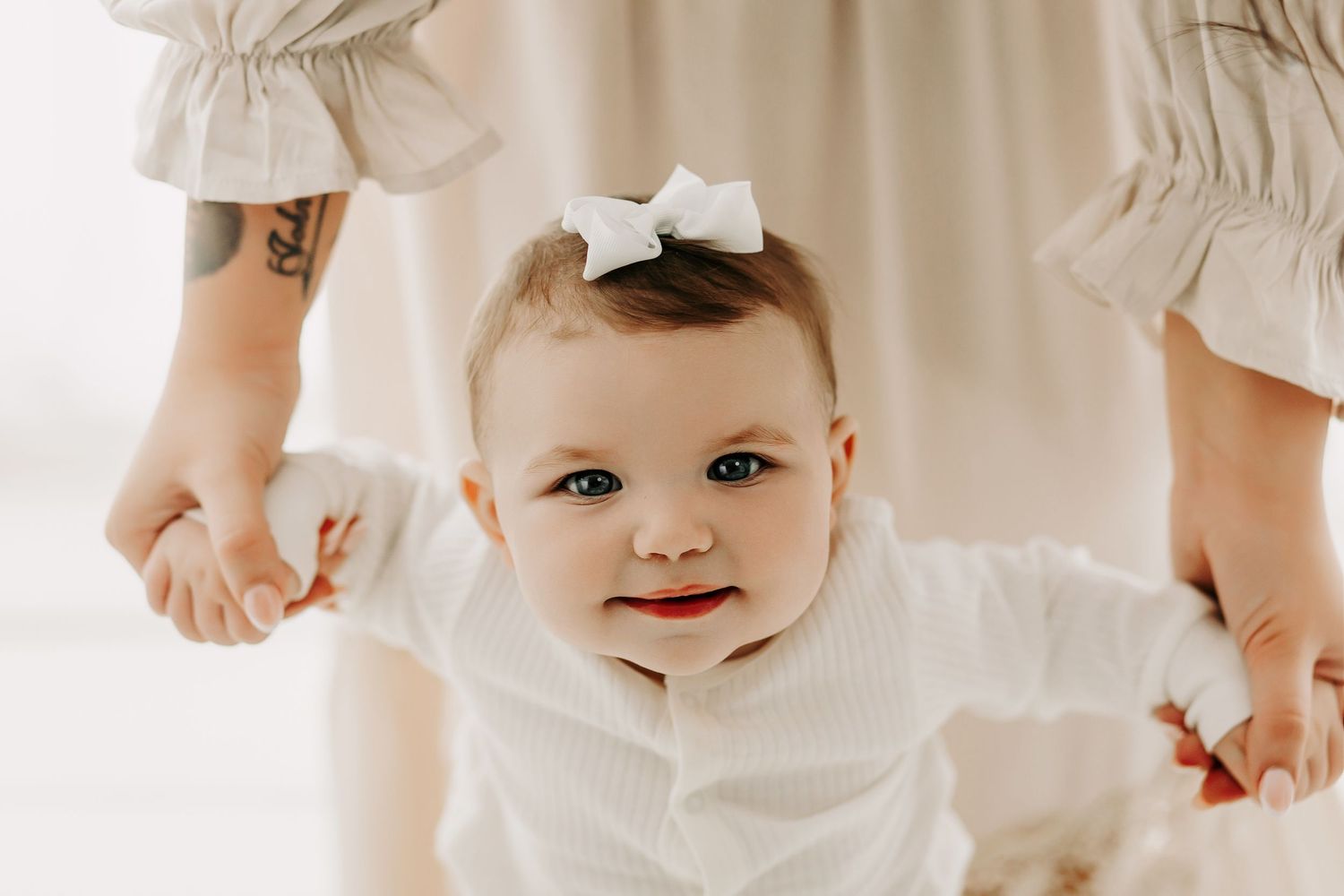 Baby with white bow smiling at camera while being held by parents.