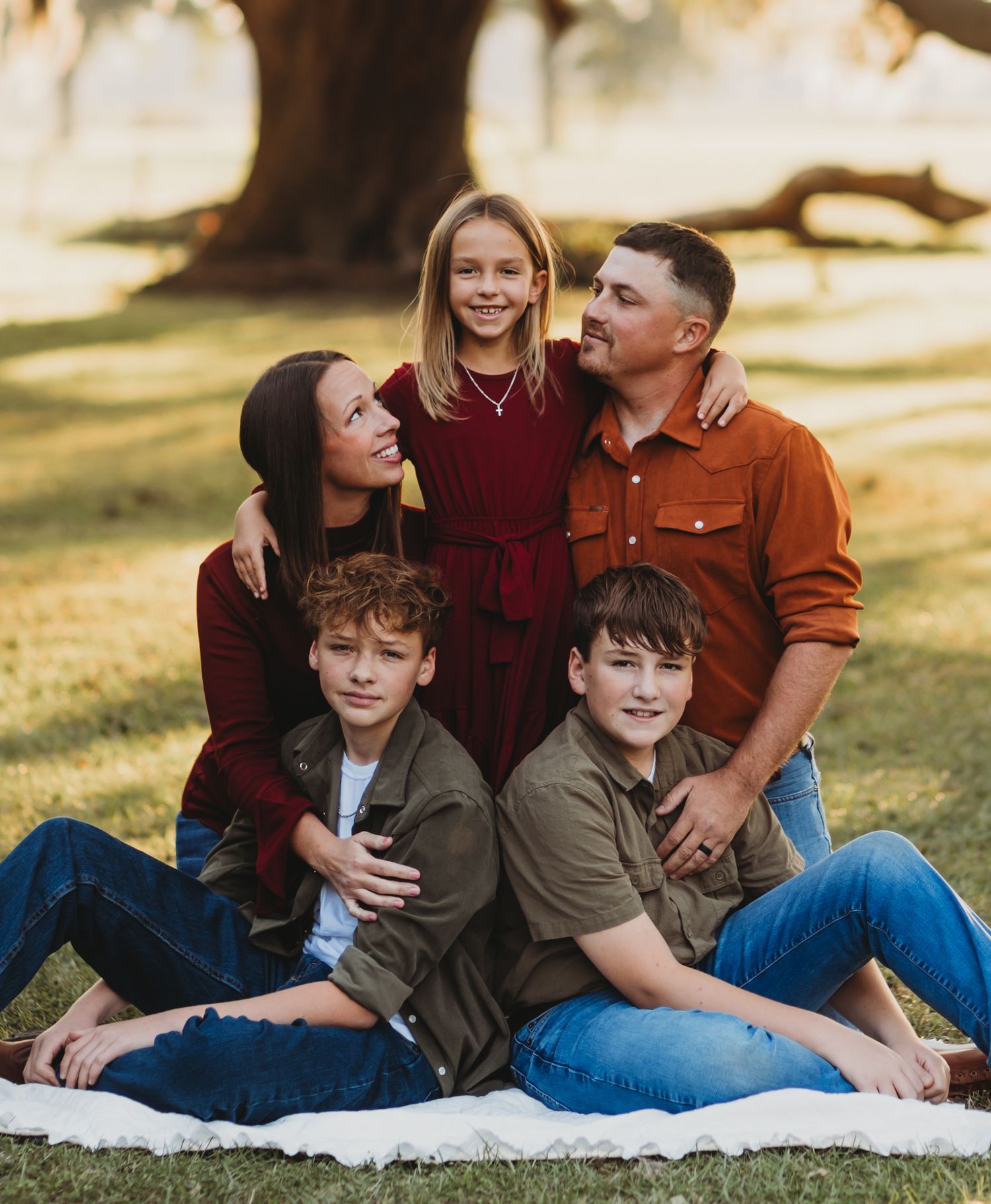 Casual family portrait session with parents and children sitting on blanket under tree.