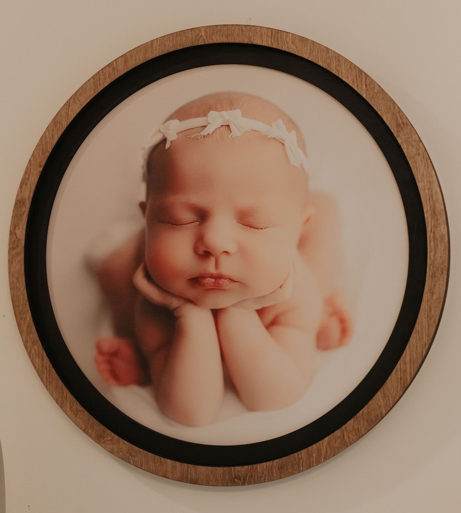 Artistic newborn portrait in a wooden circular frame showing a sleeping baby.