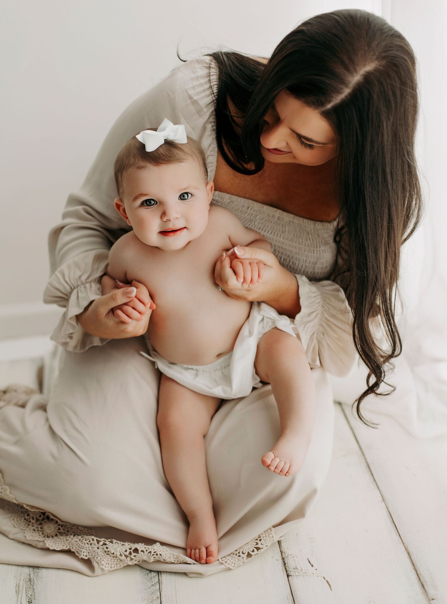 Mother and baby in white outfits share tender moment during studio photo session.