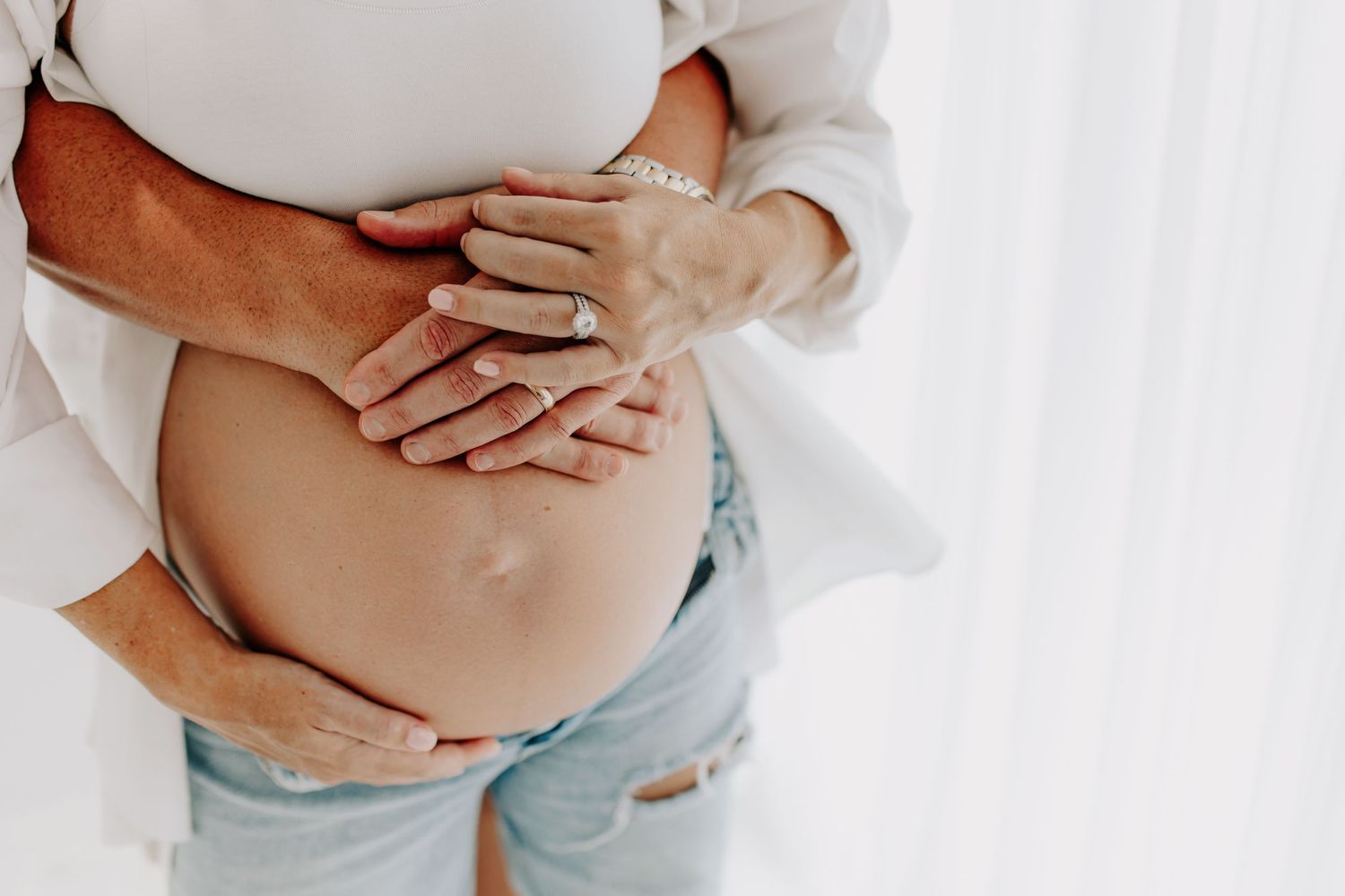 Close-up of pregnant woman's belly being tenderly held against white background.