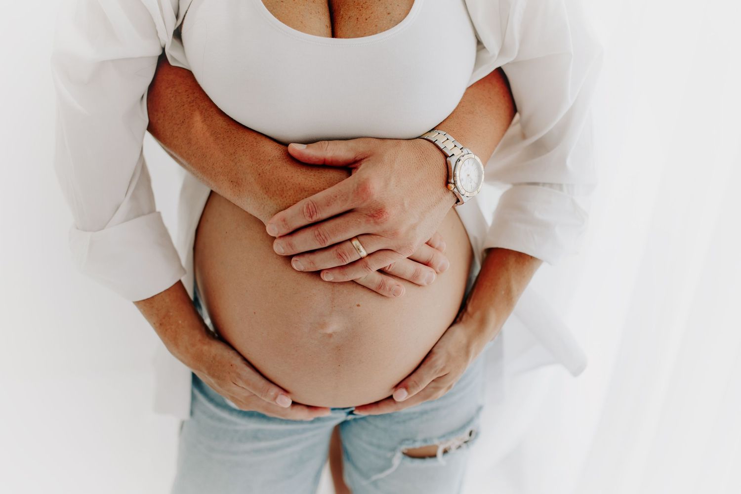 Maternity portrait showing hands embracing a pregnant belly in soft natural light.