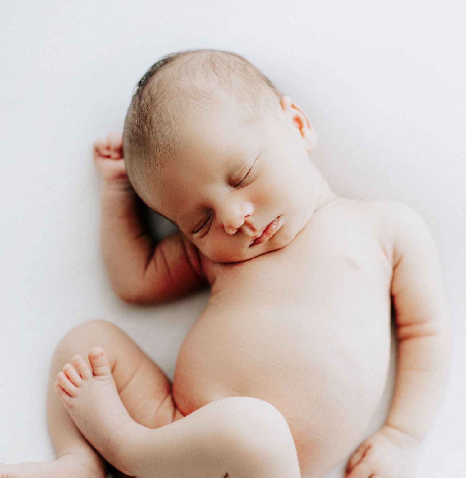 Newborn baby sleeping peacefully on white blanket in natural light.