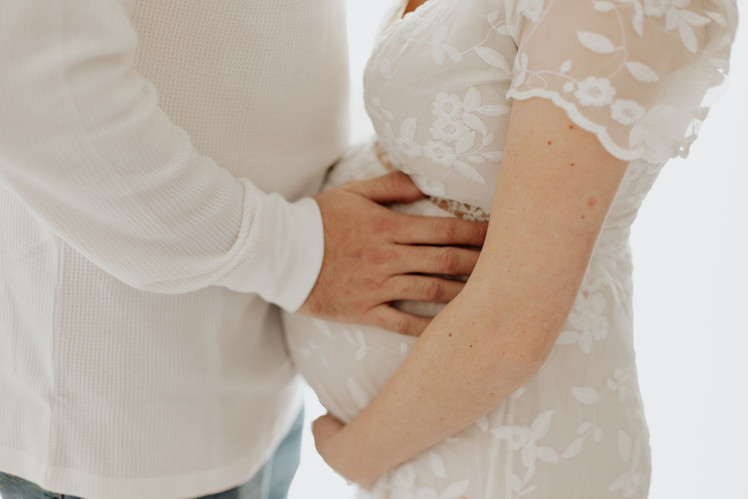 An artistic maternity photo of hands cradling a pregnant belly against a white backdrop.