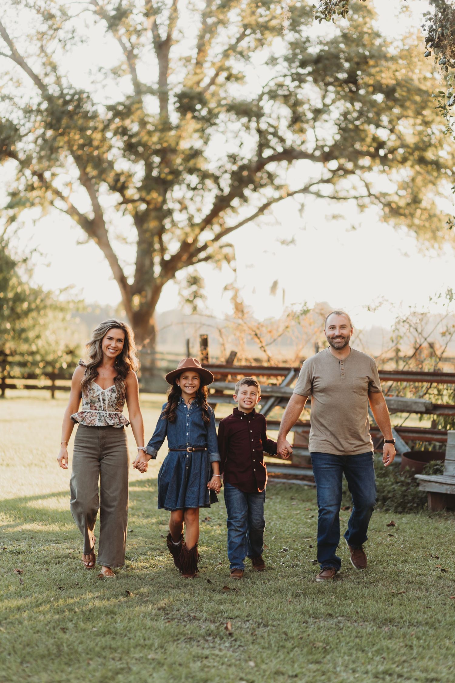 Family walking together holding hands across grassy field during golden hour photoshoot.